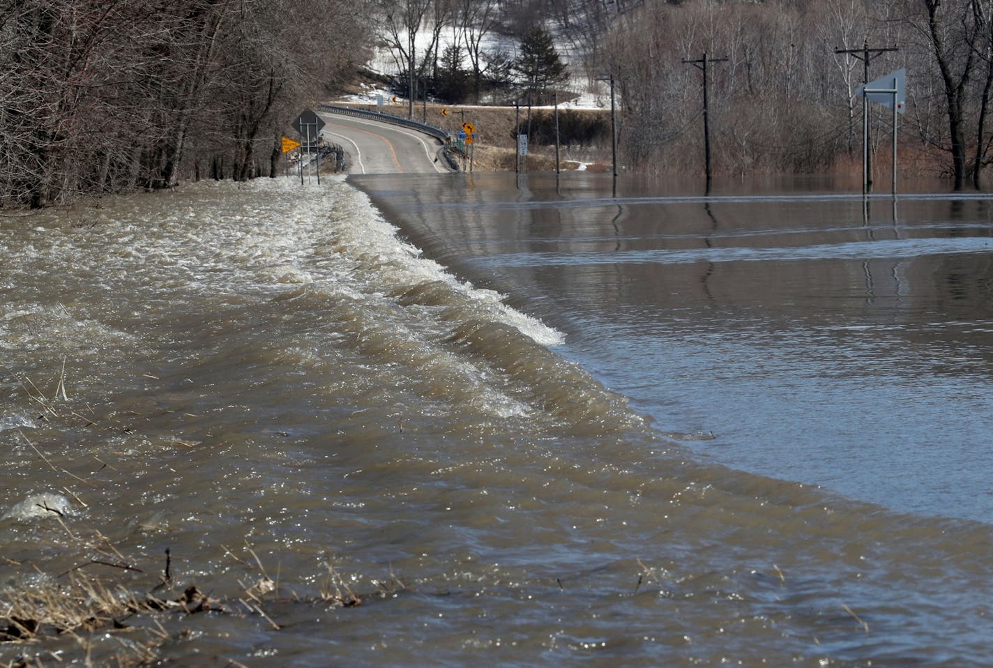 High water rushes over Highway 19 as melting snow along the Minnesota River is causing flooding and closing down three of four highways heading into town Wednesday, March 20, 2019, in Henderson, MN.