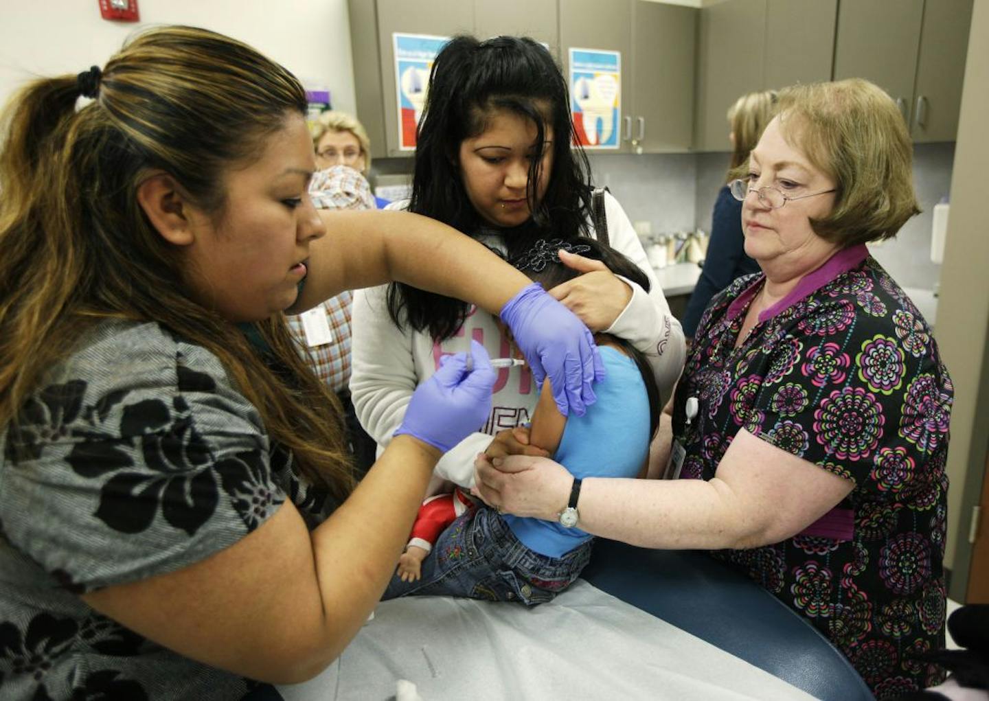 Nurses Fatima Guillen, left, and Fran Wendt, right, give Kimberly Magdeleno, 4, a Tdap whooping cough booster shot, as she is held by her mother, Claudia Solorio, Thursday, May 3, 2012, at a health clinic in Tacoma, Wash. Washington Gov. Chris Gregoire opened up an emergency fund Thursday to help contain a whooping cough epidemic in the state as officials urged residents to get vaccinated.