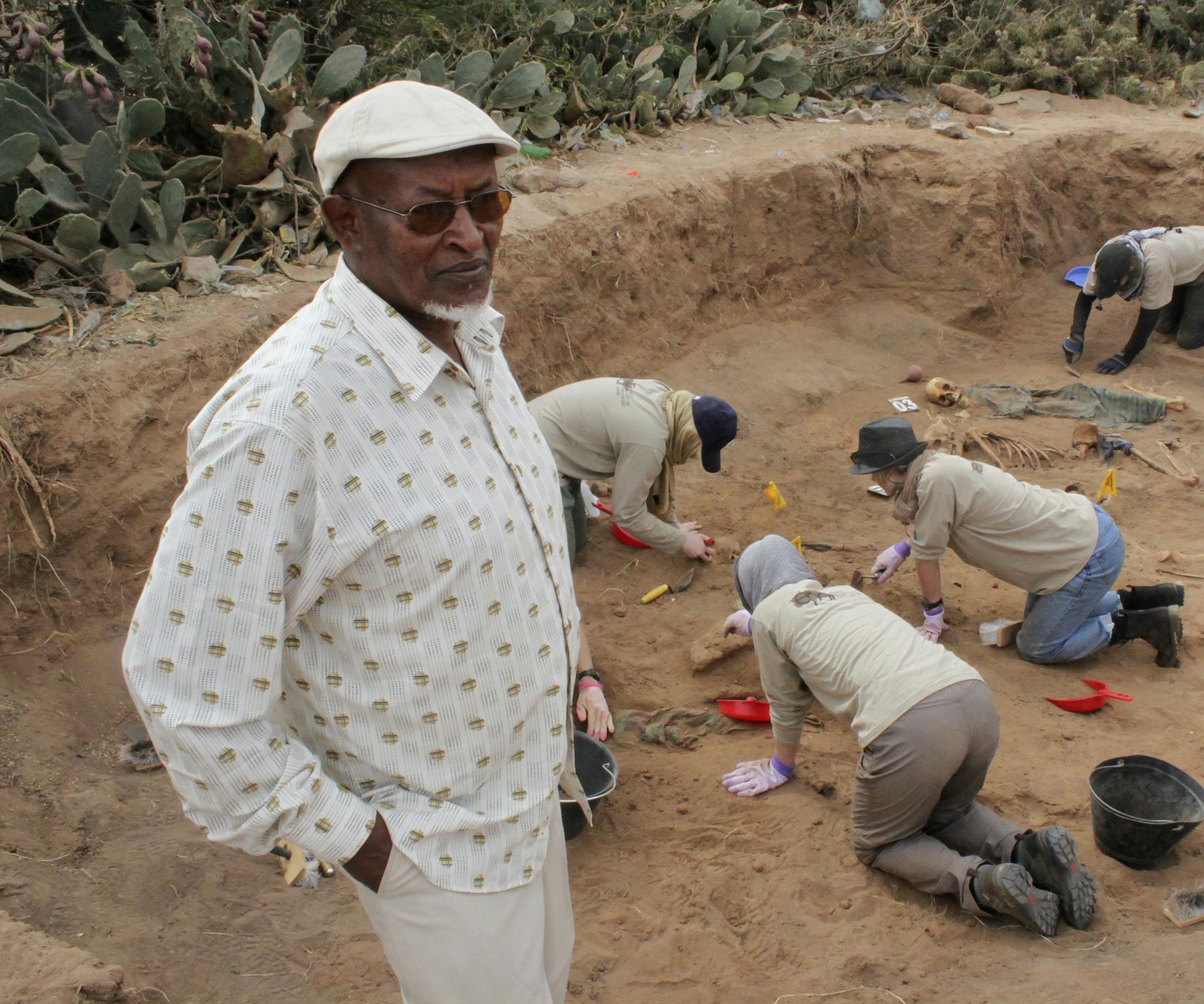 In this photo taken Tuesday, Feb. 18, 2014, Chairman of the Somaliland War Crimes Commission Kadar Ahmed, left, oversees members of the Peruvian Forensic Anthropology Team as they work to uncover bodies buried in a mass grave in Hargeisa, Somaliland, a breakaway region of Somalia. An American volunteer gently brushes away dirt to reveal the bones of a Somali victim buried in a mass grave some 30 years ago. Tens of thousands of skeletons may lie in mass graves here, on the northern edge of Somali
