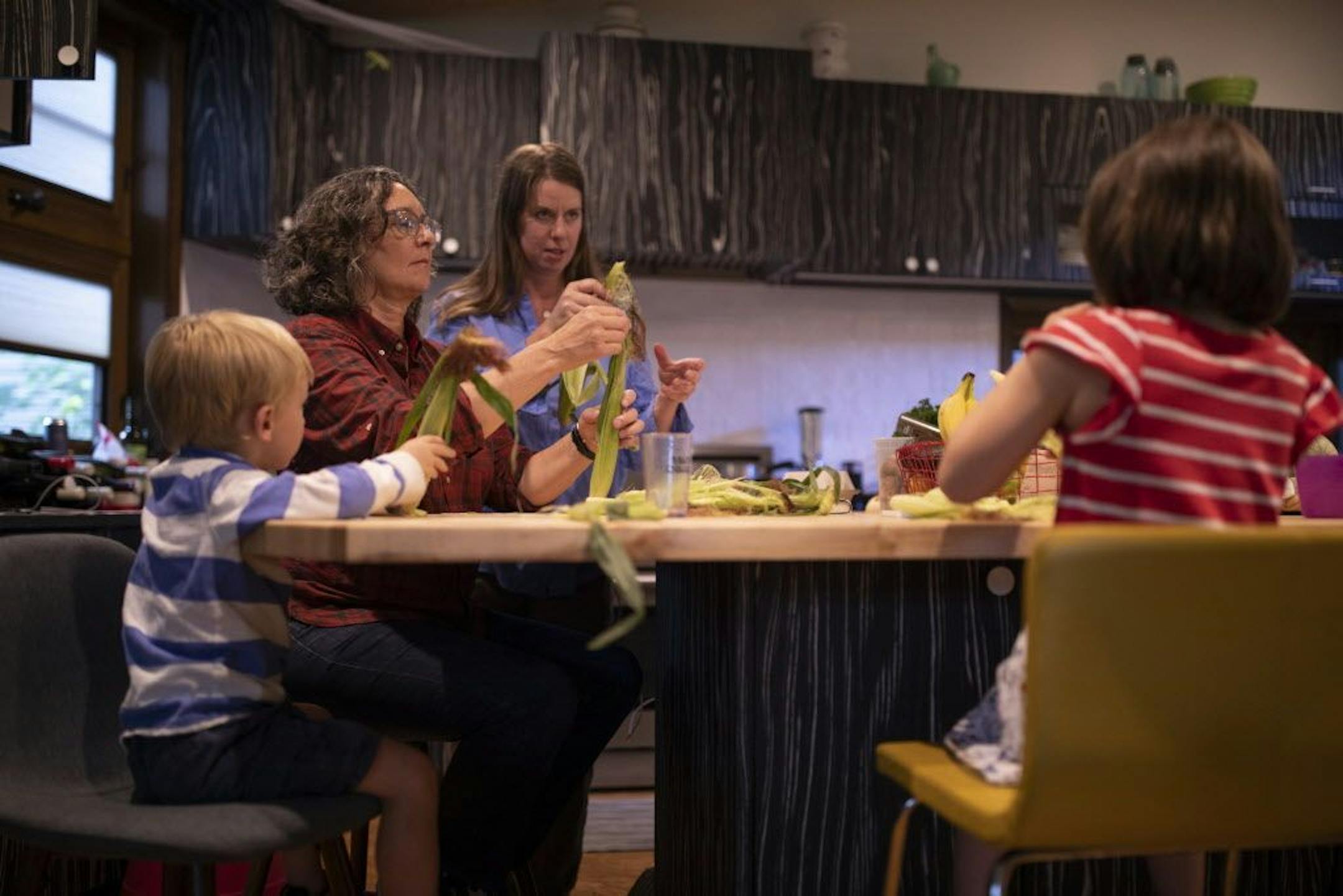Kim Bartmann and her wife, Sarah Jane Wroblewski, showed their kids, Emmitt and Elaina how to shuck corn while fixing dinner.