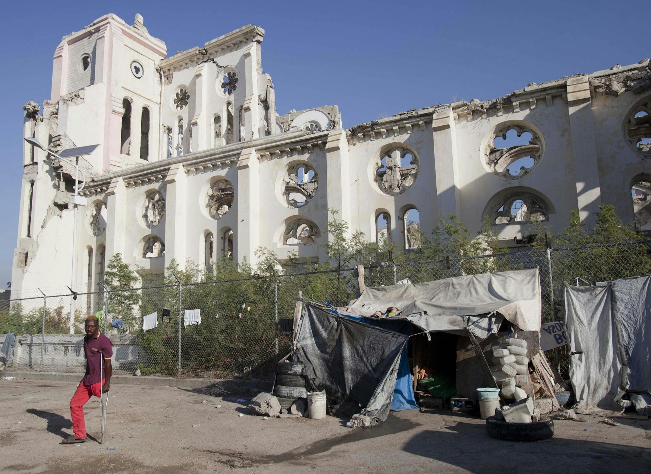 FILE - This combo of two photos shows a Jan. 12, 2010 file photo, top, of Marie La Jesula Joseph praying outside the Cathedral the day it was destroyed by a 7.0 earthquake that struck Port-au-Prince, Haiti, and a photo taken five years later on Jan. 10, 2105, that shows the structure still in disrepair. Recovery has been uneven at best, plagued by poor planning and accusations of graft. (AP Photo/Rodrigo Abd, Dieu Nalio Chery, File)