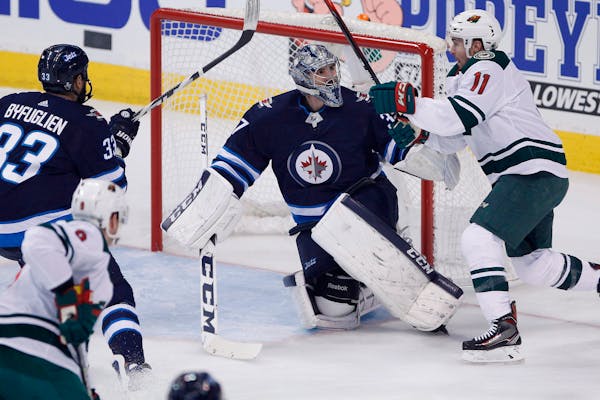 Jets goaltender Connor Hellebuyck looks up at Minnesota Wild's Zach Parise as he saves a shot during the first period of Game 1