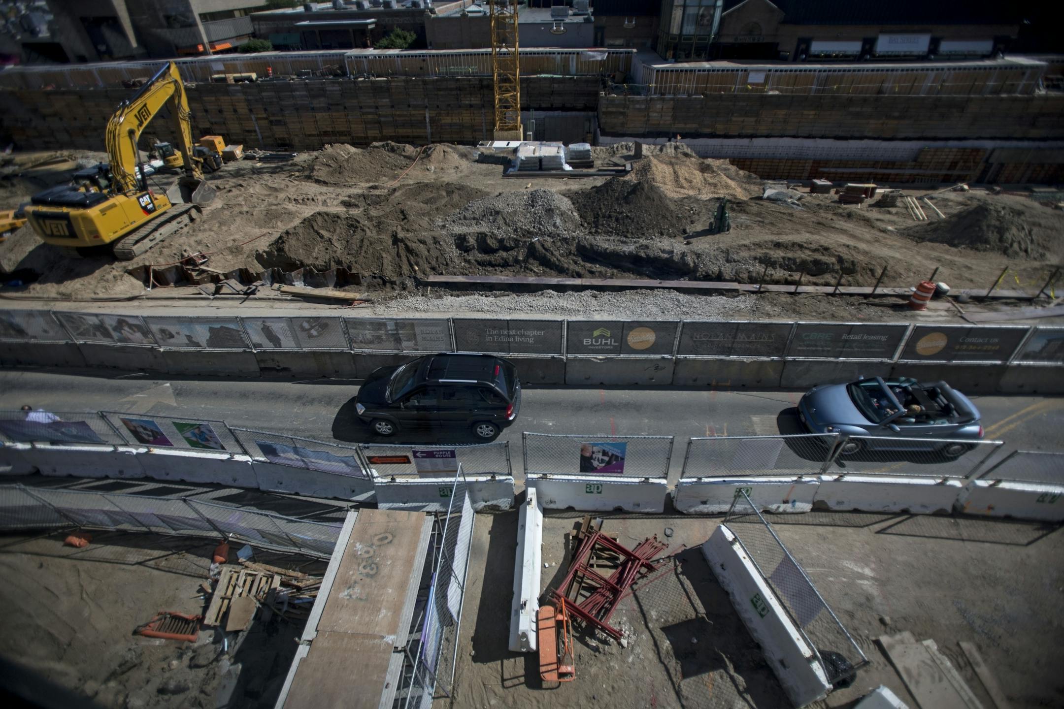 Cars drive in the street gap between the construction sites for a new apartment and renovated parking ramp.