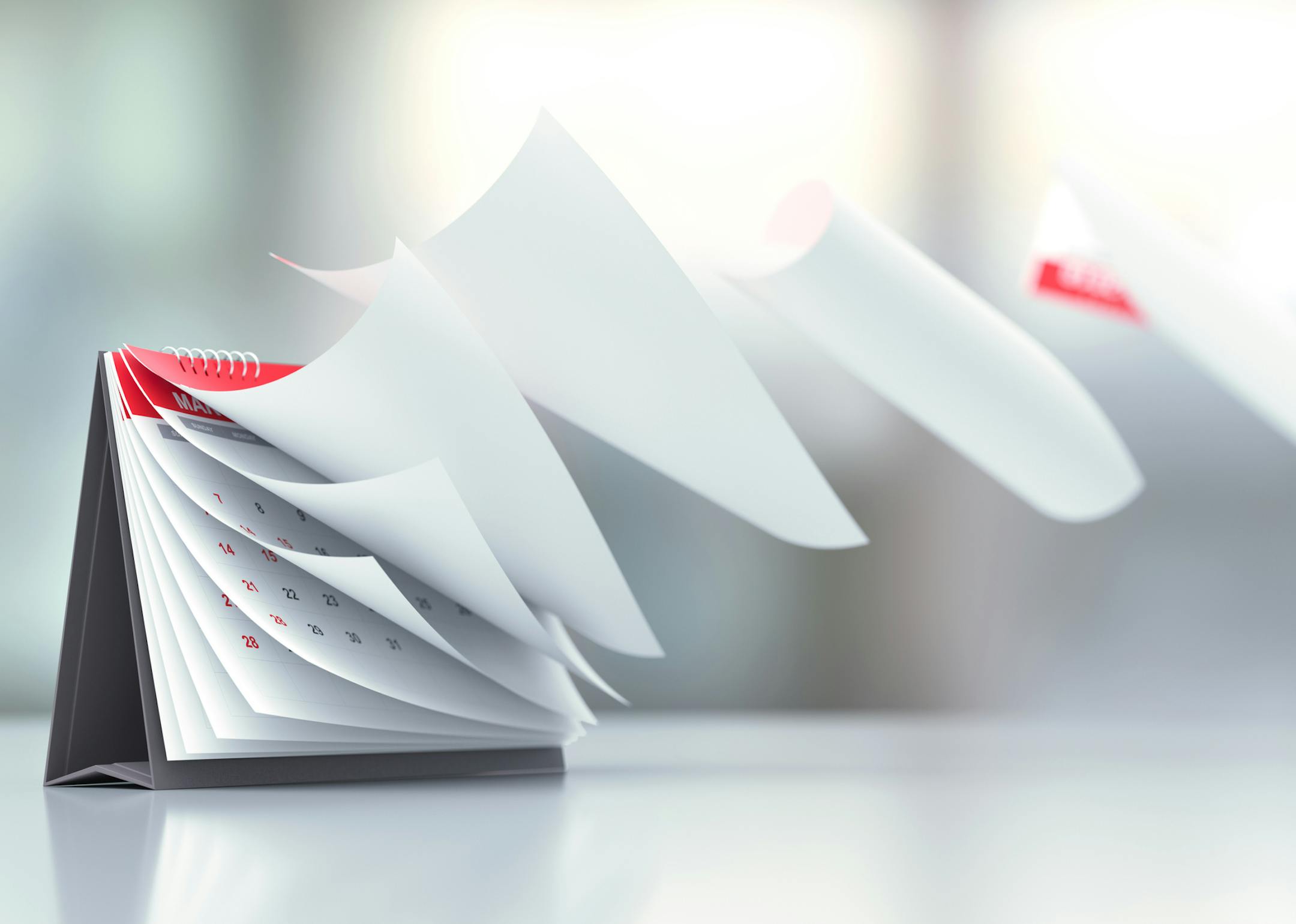 Pages of a red calendar standing over defocused background are flying away. Horizontal composition with copy space. Calendar and reminder concept with selective focus.