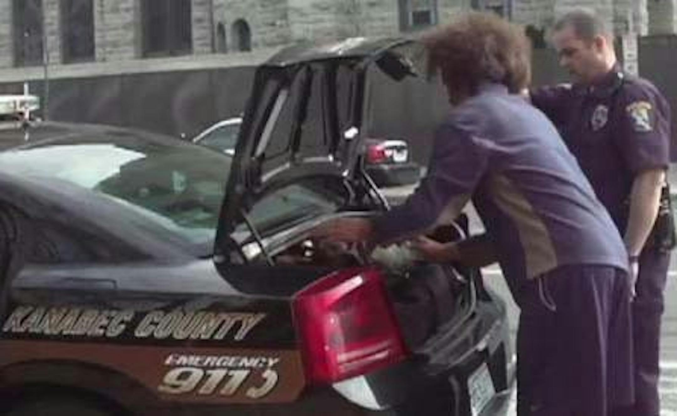 This still from a video presented at a Minneapolis City Council meeting shows an Occupy activist putting his luggage into a police car. The video is by Twin Cities Indymedia, Rogue Media, Communities Against Police Brutality, and Occupy Minneapolis.