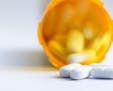 close up of a group of white tablets with an out of focus prescription bottle in the background