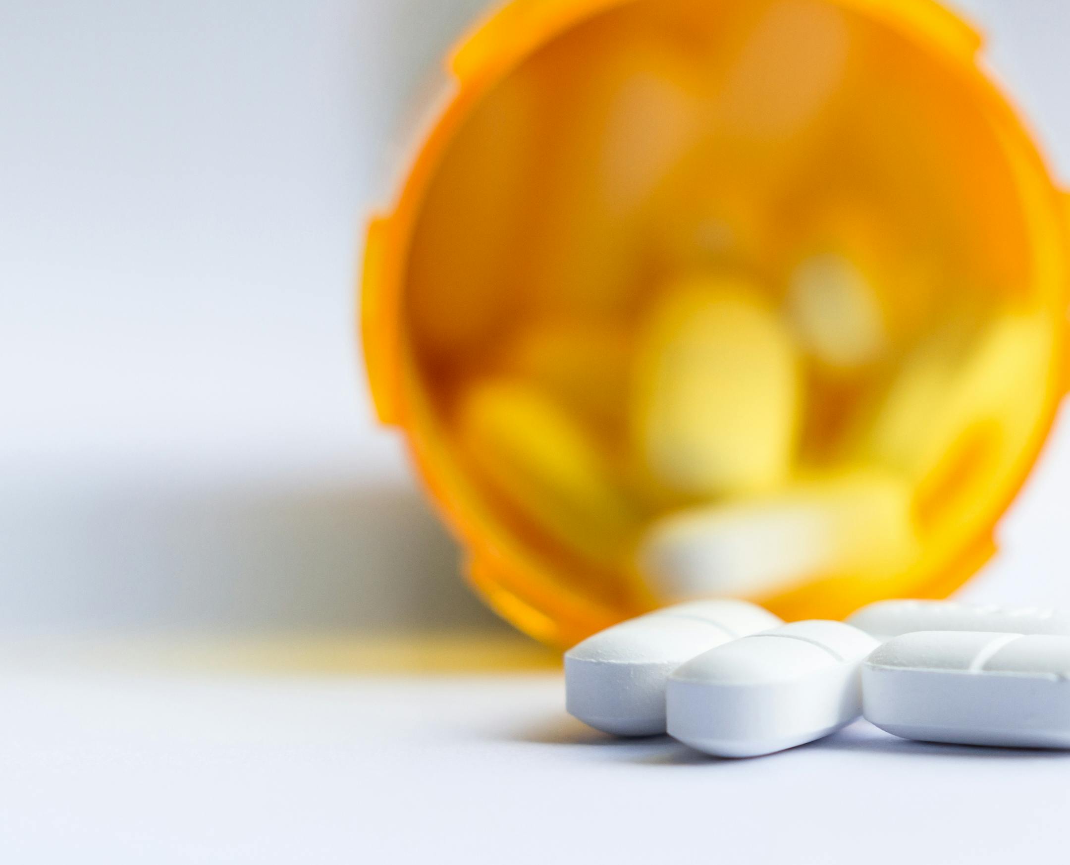 close up of a group of white tablets with an out of focus prescription bottle in the background