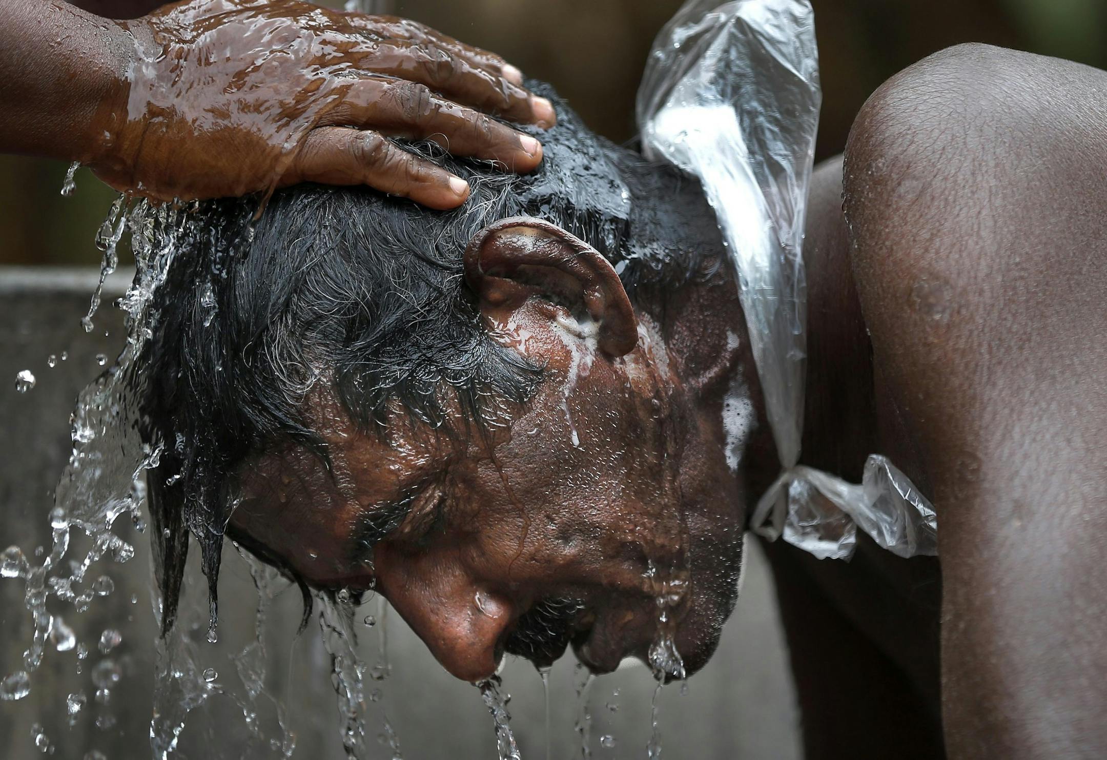 In this July 16, 2013 photo, Kumaradasa, a Sri Lankan farmer suffering from a chronic kidney disease of unknown etiology, bathes helped by his wife outside their house in Medavachchiya, Sri Lanka. The cause of his disease, which affects anywhere from an estimated 70,000 to 400,000 people in Sri Lanka's rice basket, remains an enigma without a name. Kumaradasa died on June 8, 2014. (AP Photo/Eranga Jayawardena)
