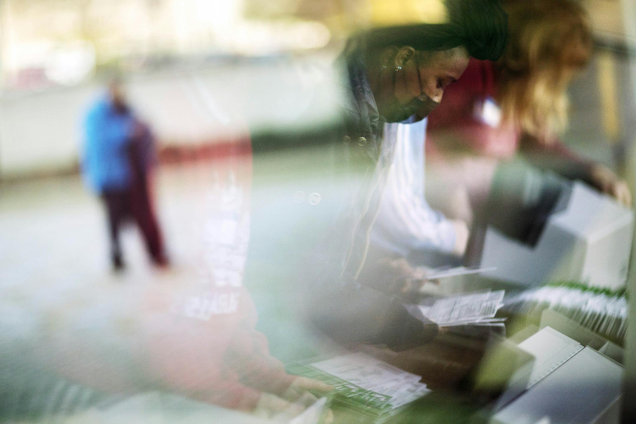 Election inspectors are reflected in a window at right as they begin processing ballots while a voter outside arrives to drop off a ballot at an official drop-off box on Election Day at City Hall in Warren, Mich., in Macomb County, Tuesday, Nov. 3, 2020. (AP Photo/David Goldman)