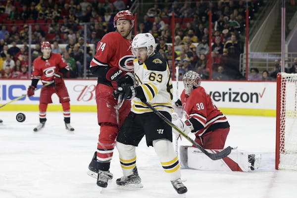 Boston Bruins' Brad Marchand (63) chases the puck with Carolina Hurricanes' Jaccob Slavin (74) as Hurricanes goalie Cam Ward keeps an eye on the puck 