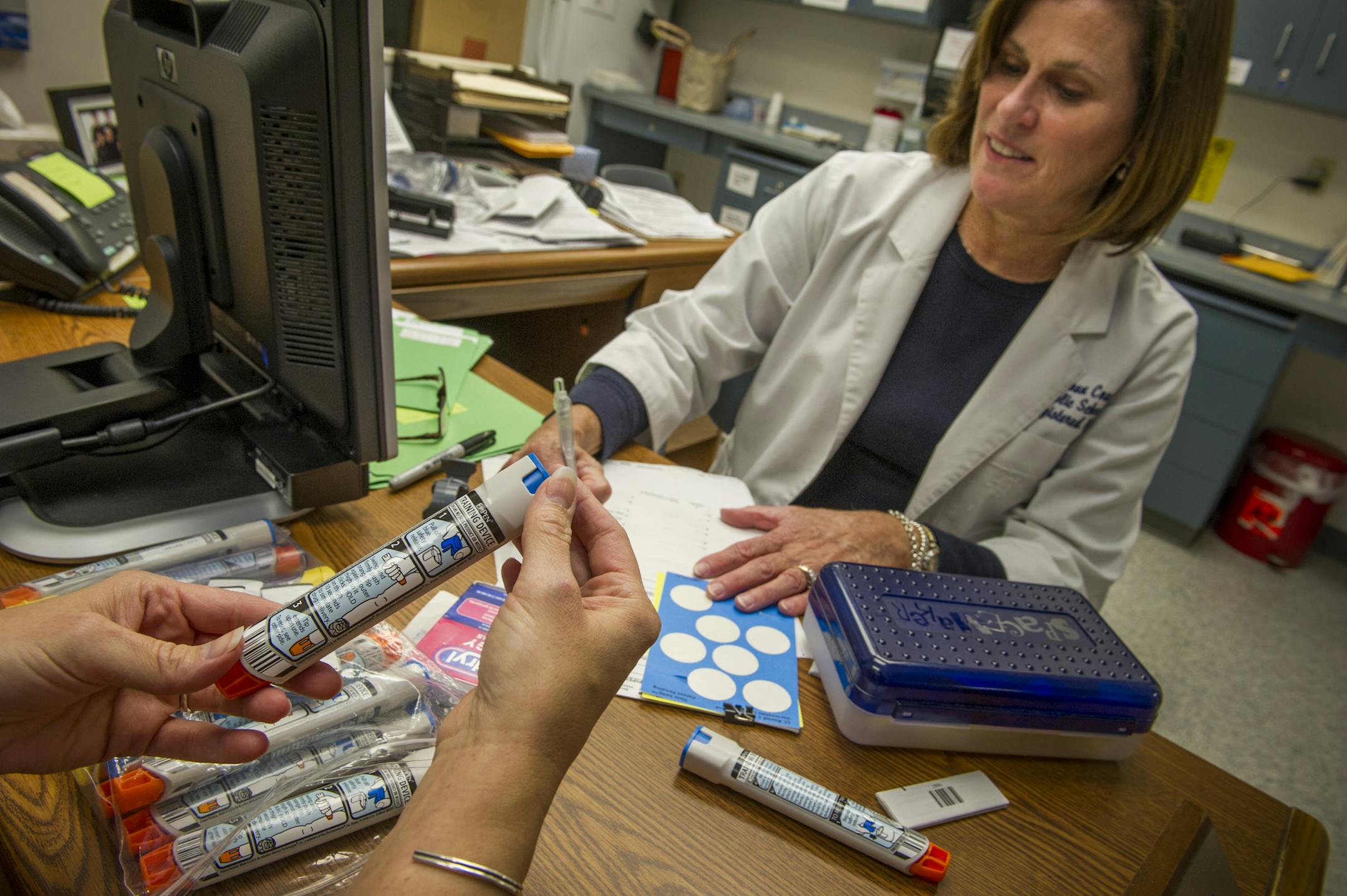 FILE-- Diane Voelker, a school nurse, and her assistant, Beth Little, look over EpiPens at Stone Bridge High School in Ashburn, Va., Aug. 31, 2012. In another move to quell outrage over its price increases, the maker of the EpiPen said on Aug. 29, 2016, that it would introduce a generic version of the product, with a price about half of the existing EpiPen&#x2019;s. The generic would be available in several weeks and be identical to the existing product, which is used to treat severe allergic re