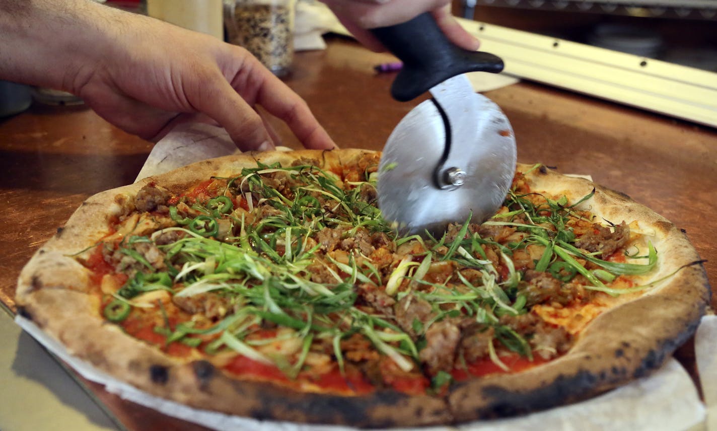 At Pizzeria Lola, pizza chef Bishara Sahoury slices the Lady Za Za pizza -- a kim chi based pizza made with Italian red sauce, house-made kimchi, Korean sausage, serrano peppers, scallions and sesame and soy chilli glaze Friday, April 11, 2014, in Minneapolis, MN.]](DAVID JOLES/STARTRIBUNE) djoles@startribune.com Story on the popularity of a Korean cabbage food - from gourmet pizza to a general mills product - owner Ann Kim offers a pizza made with it.**Bishara Sahoury,cq