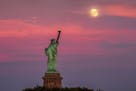 The full moon rises behind the Statue of Liberty at sunset in New York City, Monday, July 15, 2019, on the night before the 50th anniversary of the Ap