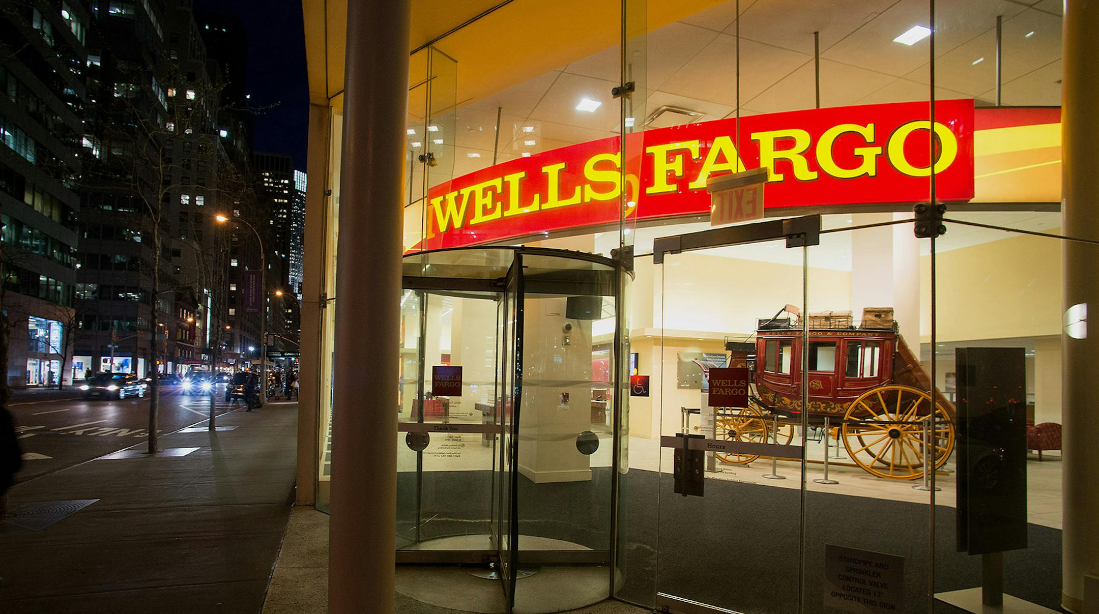 Pedestrians pass in front of a Wells Fargo & Co. bank branch at night in New York, U.S., on Monday, April 7, 2014. Wells Fargo & Co. is expected to release earnings figures on April 11. Photographer: Craig Warga/Bloomberg ORG XMIT: 484389669