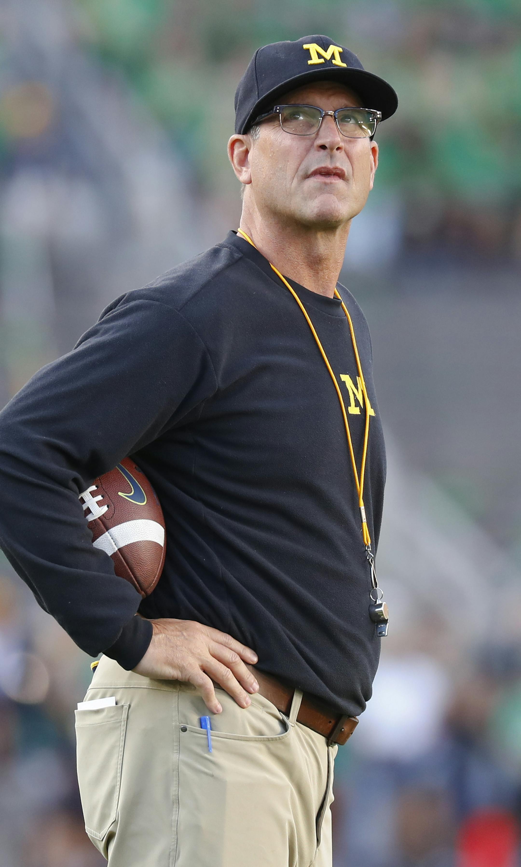 FILE - In this Sept. 1, 2018, file photo, Michigan coach Jim Harbaugh stands on the field before the team's NCAA college football game against Notre Dame in South Bend, Ind. Harbaugh says he is staying at Michigan, responding to speculation he's returning to the NFL. The former San Francisco 49ers coach tells ESPN he's not going anywhere. Fox Sports analyst Cris Carter has said Harbaugh is a potential candidate to lead Green Bay and Cleveland. Michigan won 10 games this season for the third time