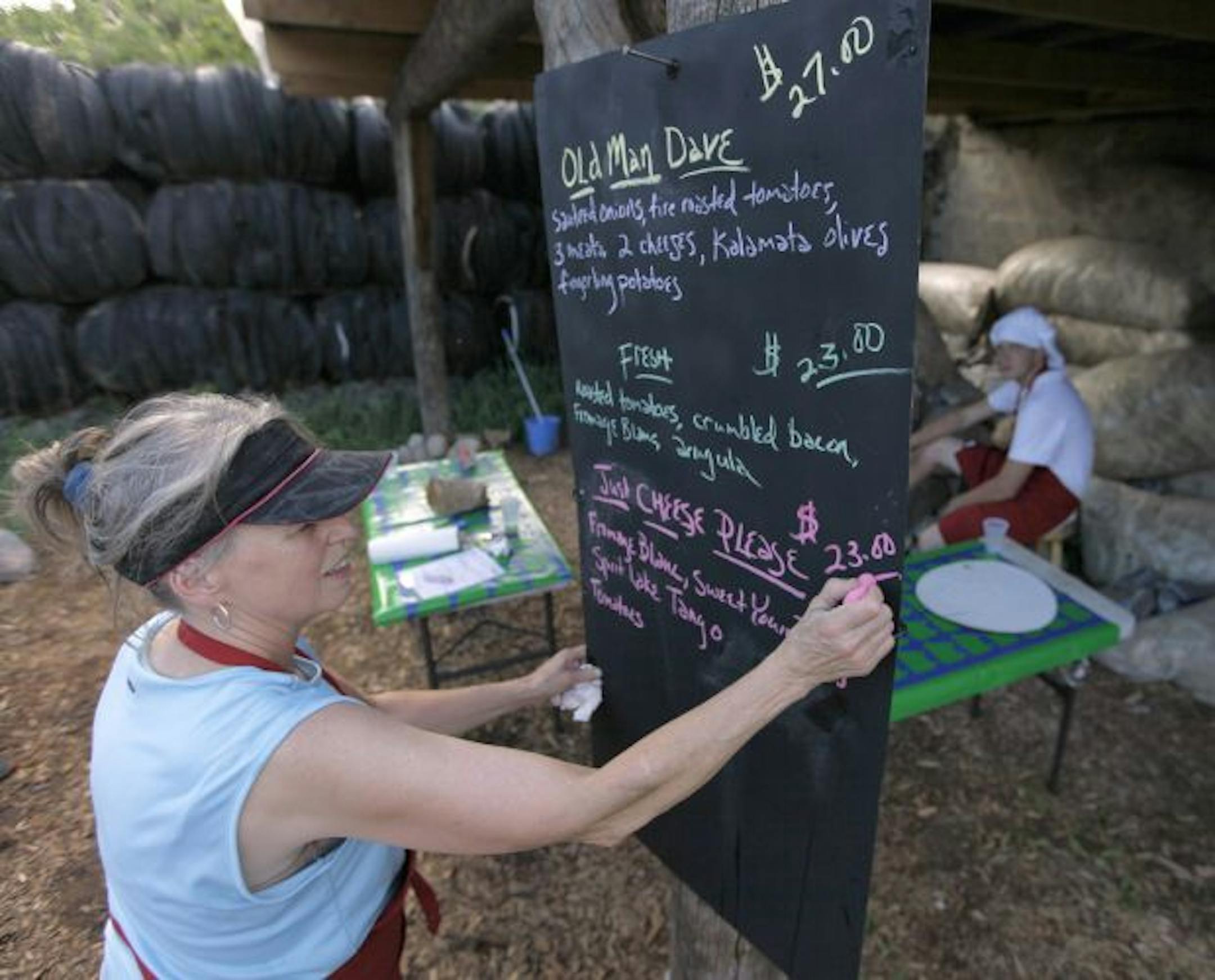 Mary Falk posts the night's pizza menu at their rustic once-a-week backyard restaurant.