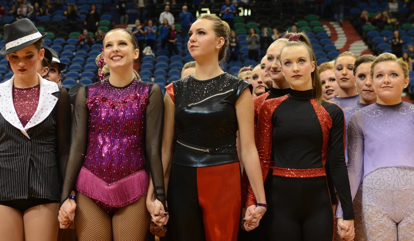 Lakeview South, Eastview, Eden Prairie, Wayzata, and Chaska dance teams all hold hands in protest prior to the announcement of placements for the 3AAA state dance team high kick division tournament in March at Target Center.]