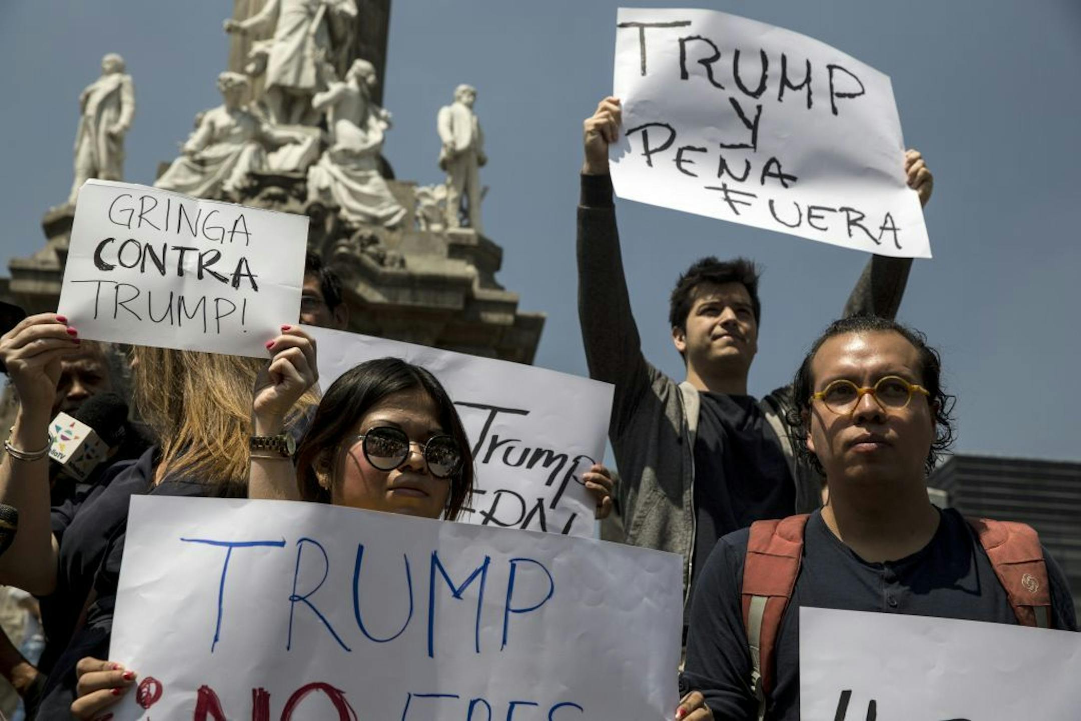 Demonstrators hold signs at the Angel of Independence monument in downtown Mexico City as Donald Trump traveled there, Aug. 31, 2016. President Enrique Pena Nieto is being criticized by many Mexicans for his willingness to meet with Trump, the Republican presidential candidate who has made hostility to immigration a central plank of his campaign.
