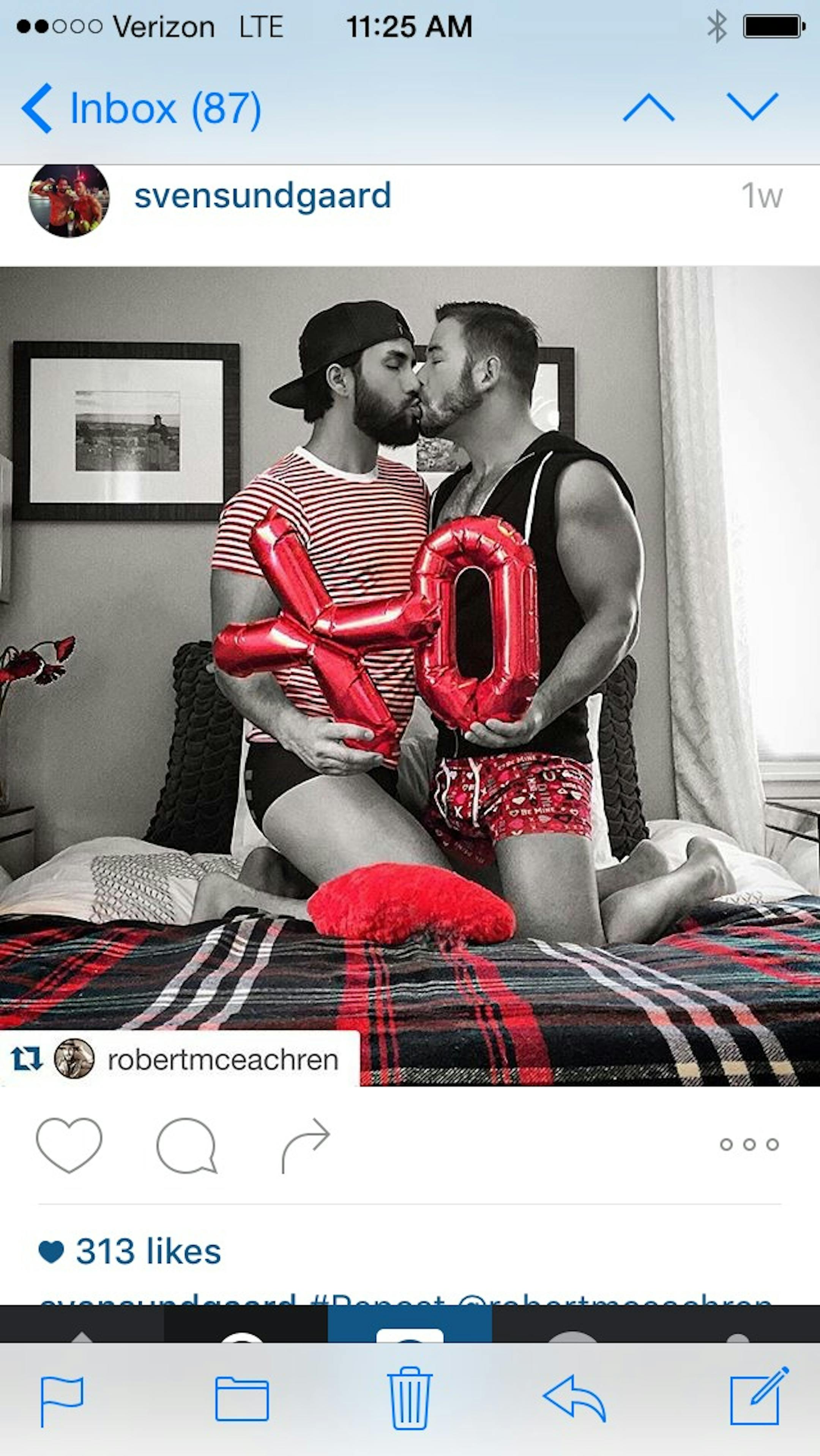 Sven Sundgaard kissing his beloved Robert. They were kneeling on a bed, Sven in Valentine's themed shorts and holding a hugs and kisses balloon.