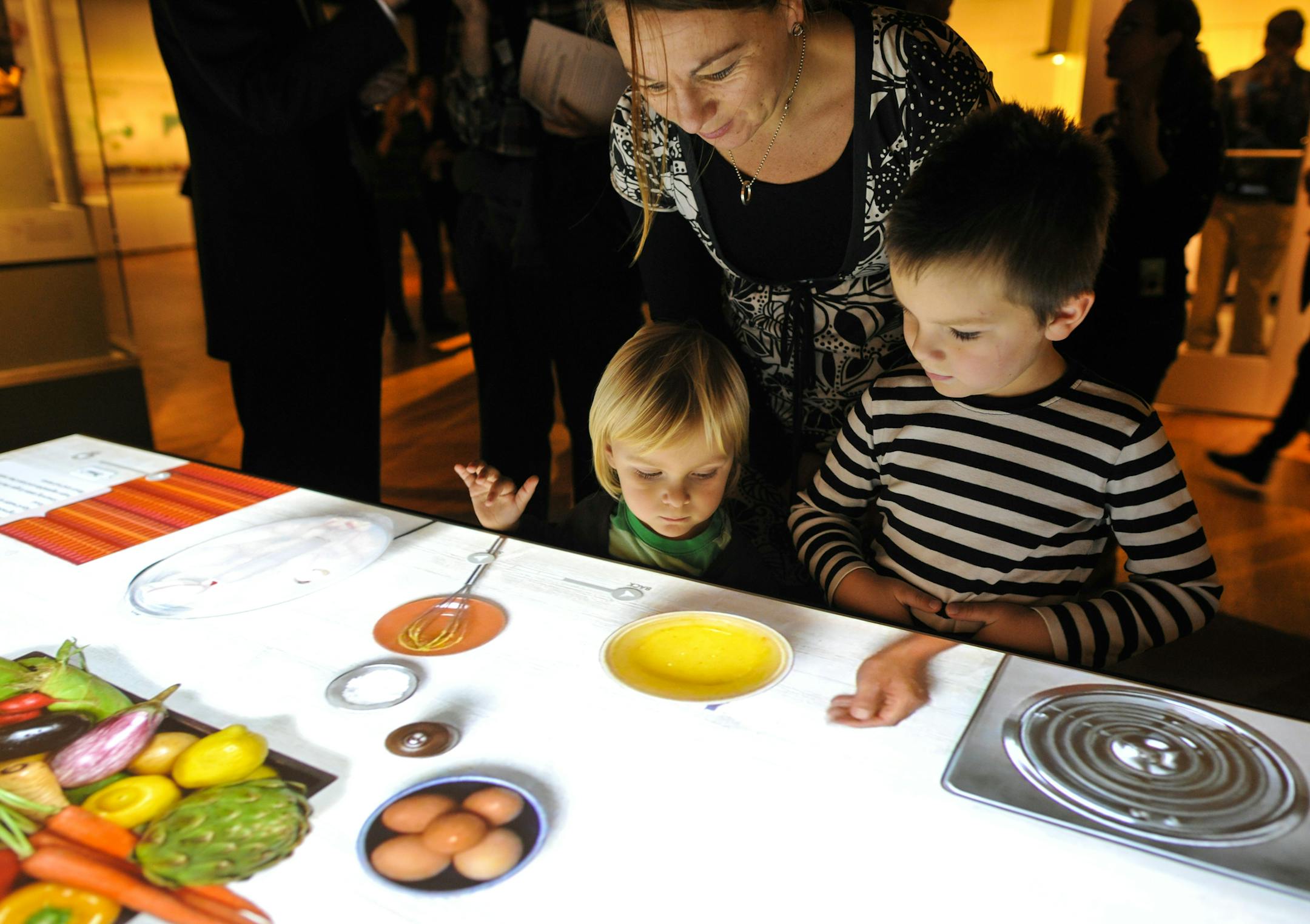 Families explore an interactive cooking table, at the Bell Museum's 'Our Global Kitchen' exhibit.