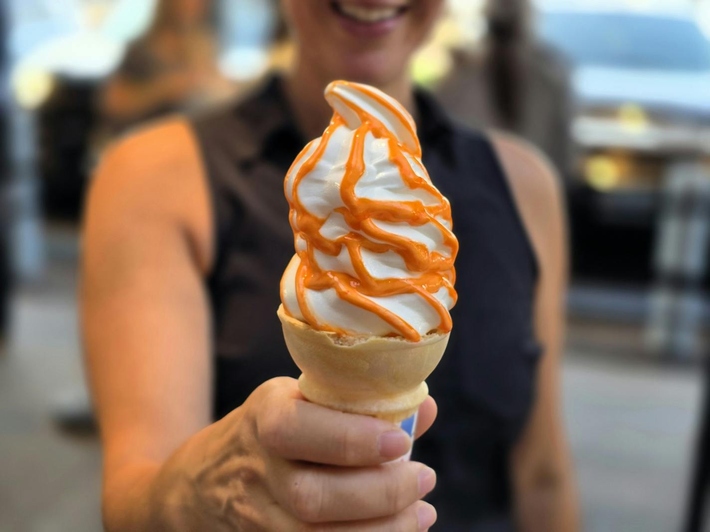 a person in a black shirt holding a cone with vanilla soft serve, twisted with orange