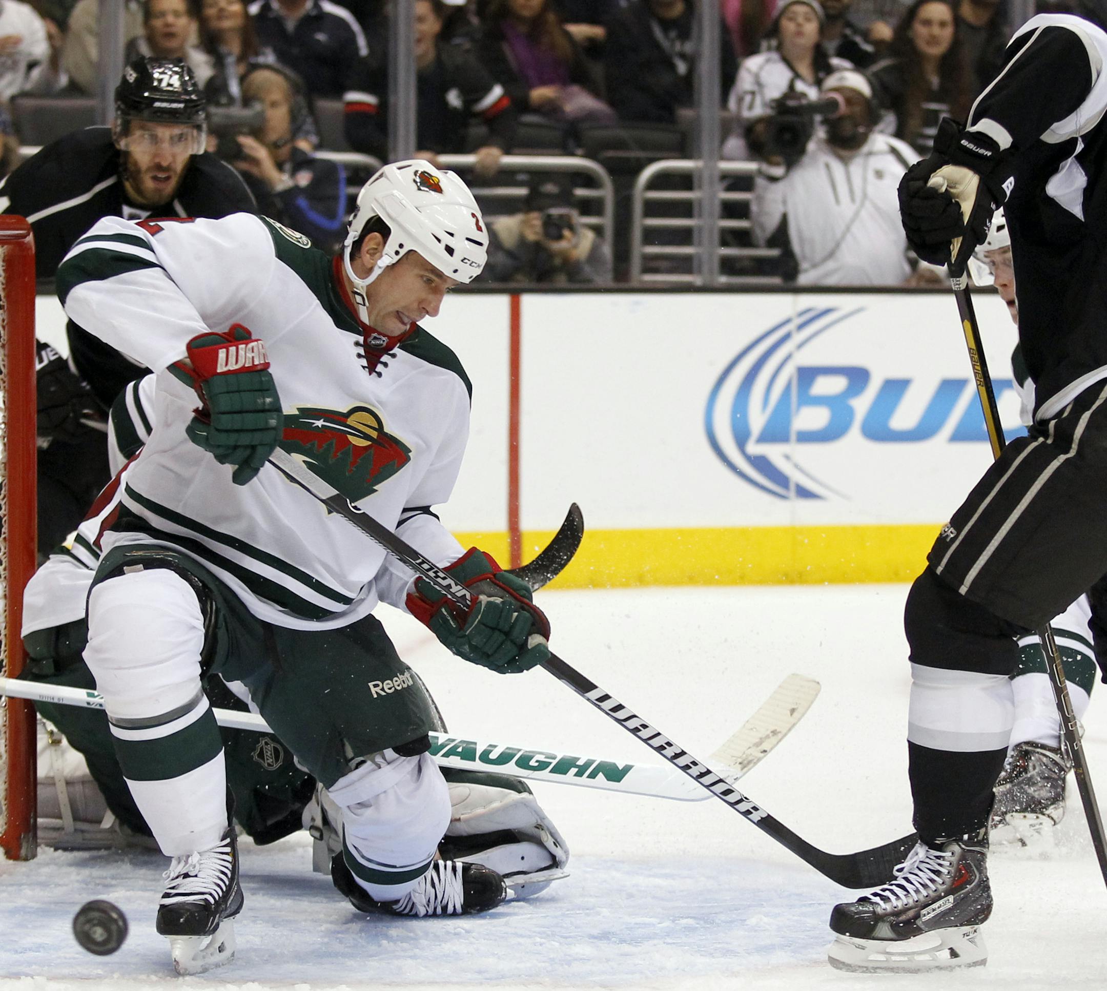 Minnesota Wild defenseman Keith Ballard, left, deflects a shot by Los Angeles Kings center Trevor Lewis, right, during the second period of an NHL hockey game Tuesday, Jan. 7, 2014, in Los Angeles. (AP Photo/Alex Gallardo)