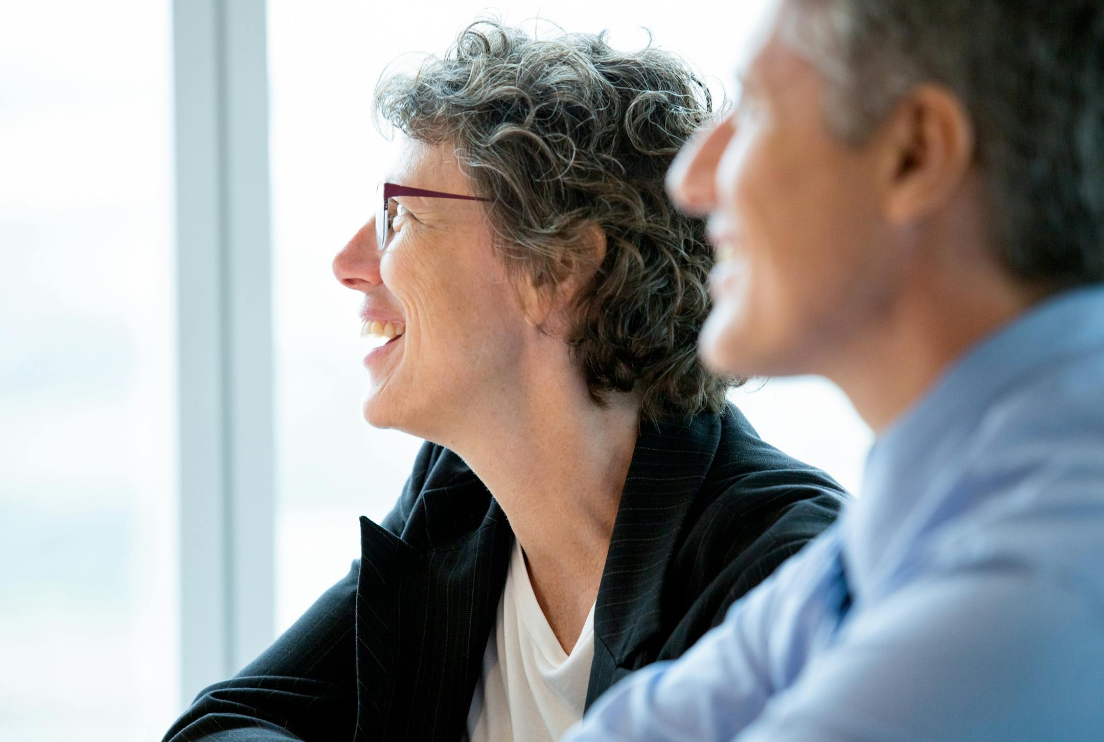 Closeup of smiling businesswoman and businessman attending meeting and looking aside with window in background. Man is blurred. Side view. istock photo