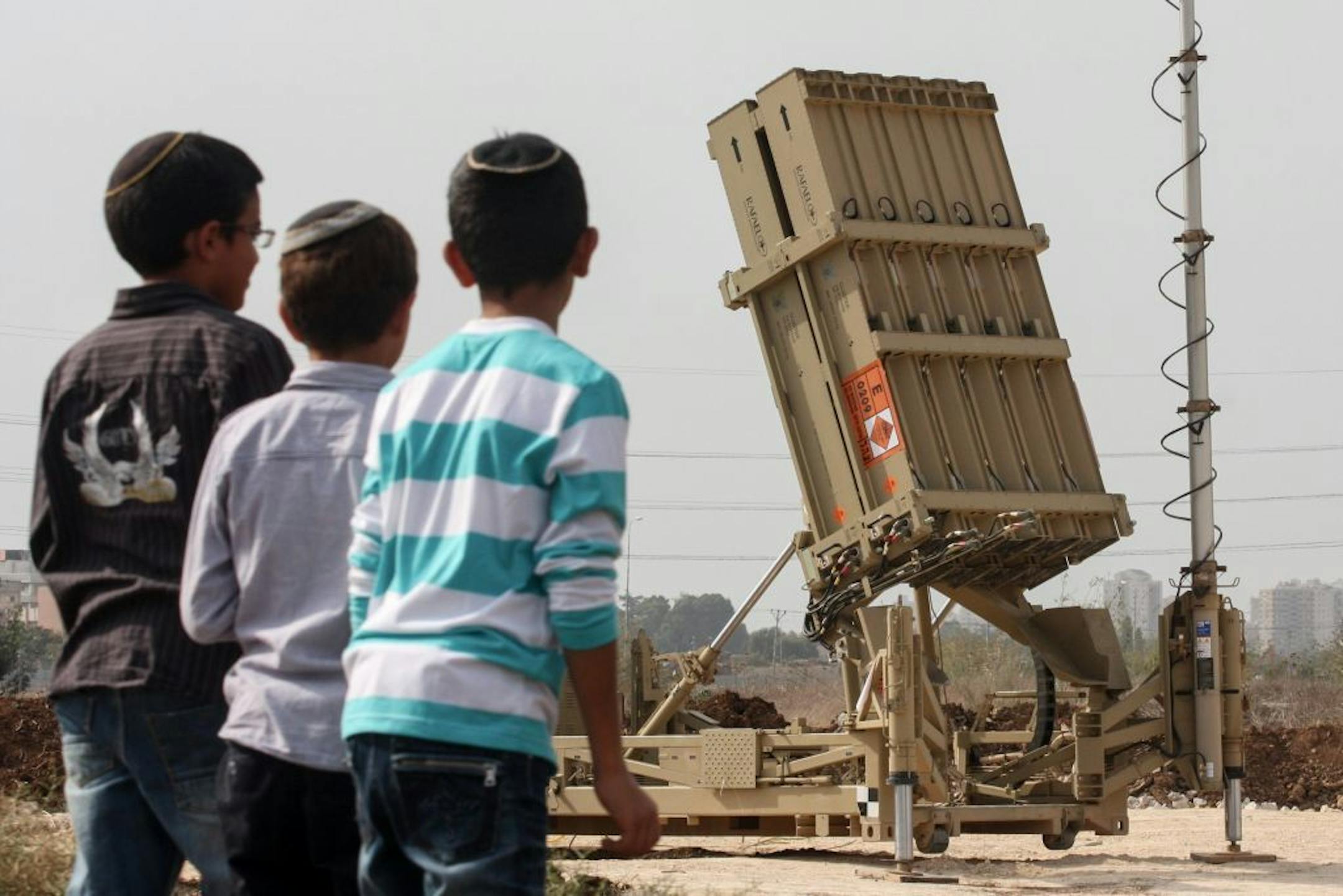 Boys look at the fifth Iron Dome anti-missile battery, deployed near Tel Aviv, Israel, on Saturday, November 17, 2012, after rocket barrages were launched at the city amid Operation Pillar of Defense. The IDF said the battery has higher interception abilities than the previous four systems already in use, and includes improved radar other upgrades.