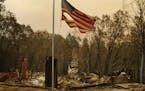 A tattered flag flies over a burned out home at the Camp Fire, Sunday, Nov. 11, 2018, in Paradise, Calif. (AP Photo/John Locher)