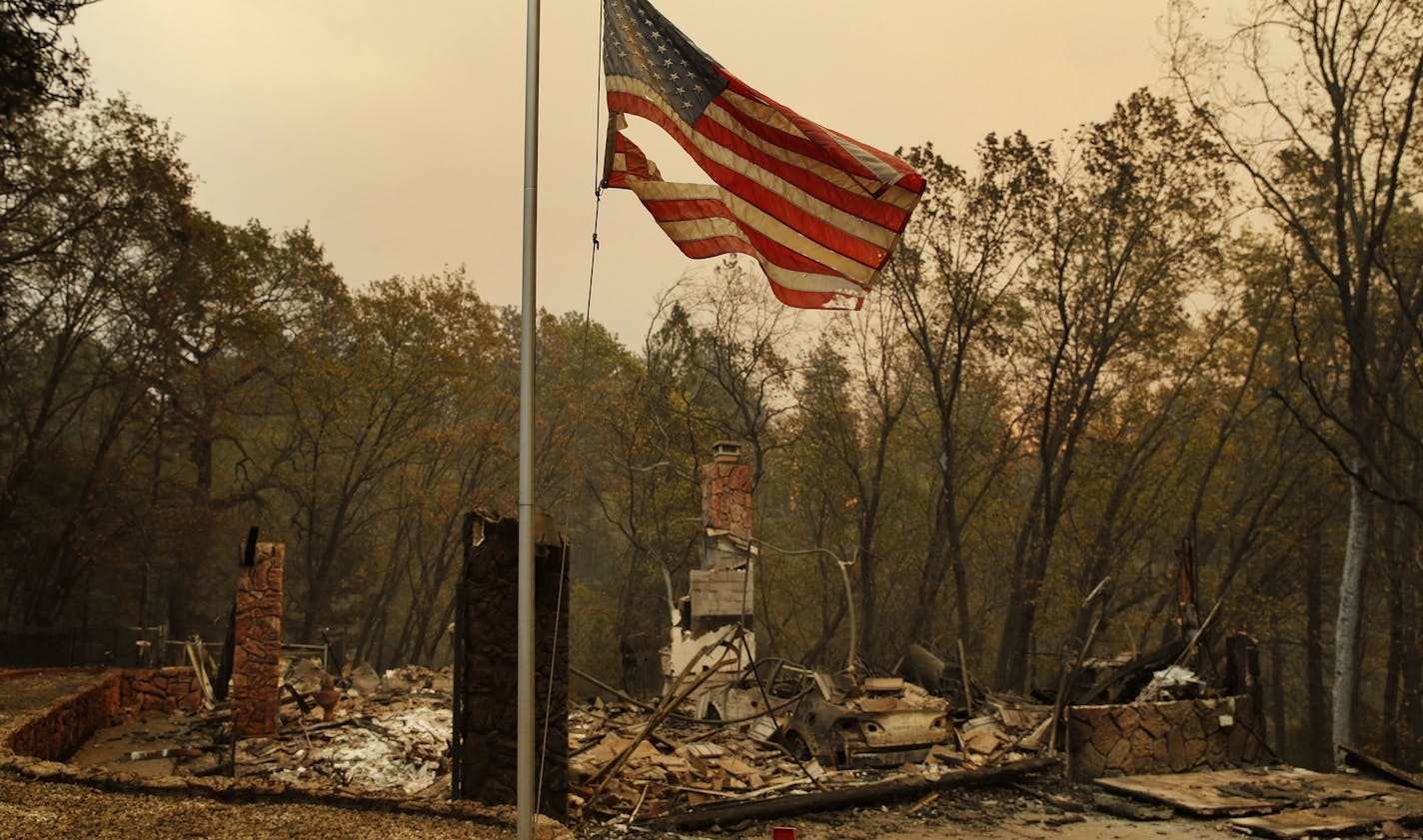 A tattered flag flies over a burned out home at the Camp Fire, Sunday, Nov. 11, 2018, in Paradise, Calif. (AP Photo/John Locher)