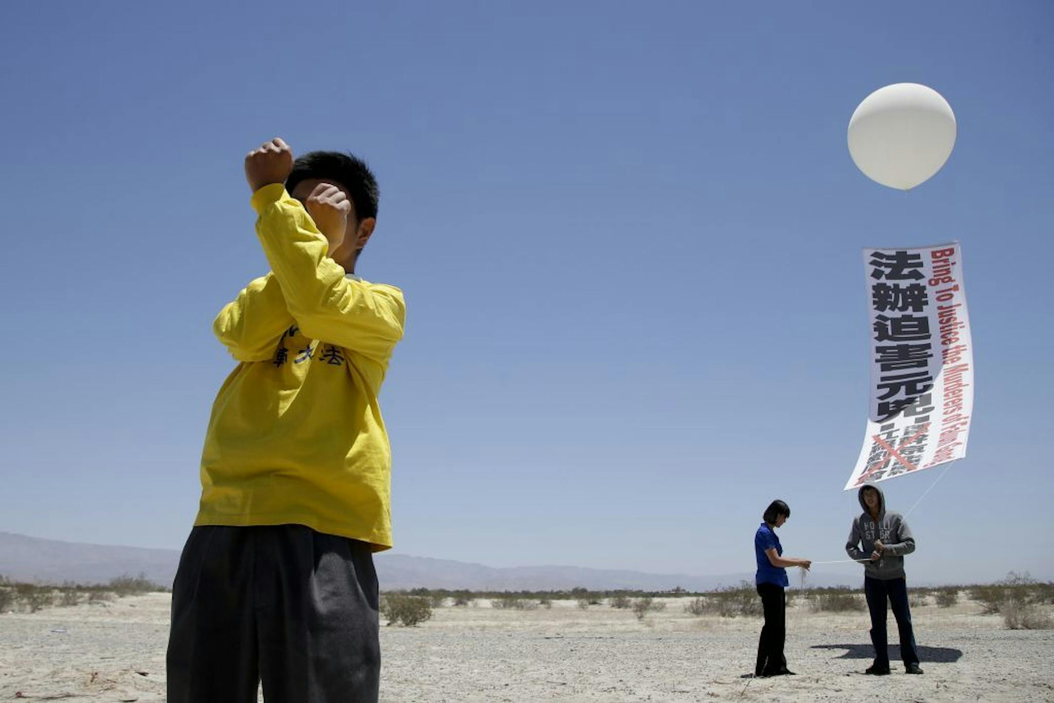 Timmy Tan, left, a member of the religious group Falun Dafa, participates in the exercise as Jun Liang, far right, and Helen Li hold a banner that reads "Bring to justice the murderers of Falun Gong" in front of the Annenberg Retreat at Sunnylands in Rancho Mirage, Calif., Thursday, June 6, 2013. The sprawling estate built by late billionaire philanthropists Walter and Leonore Annenberg in the desert east of Los Angeles is hosting two days of talks between President Barack Obama and the newly mi