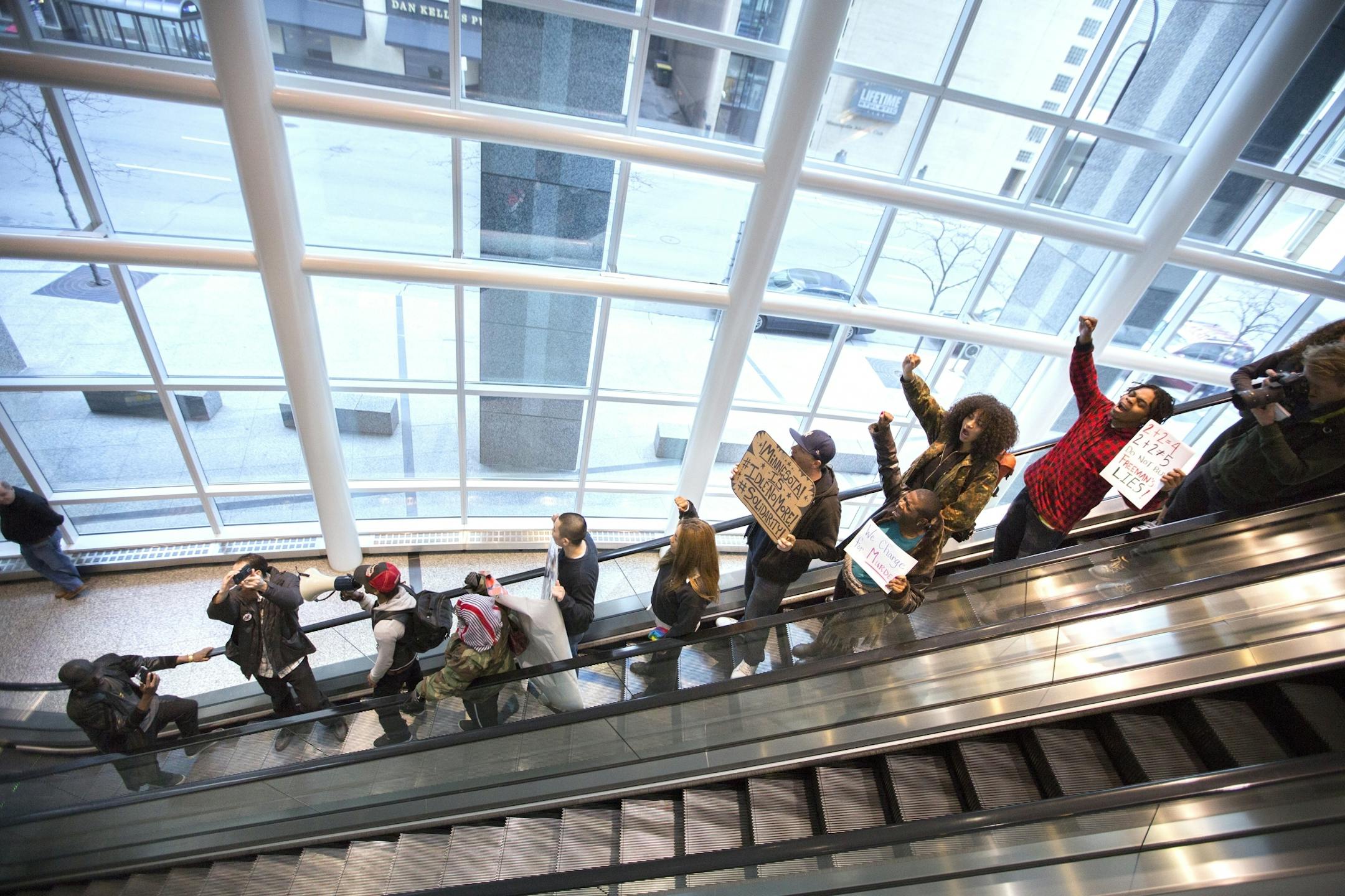 Protesters take the escalator downstairs in the Ameriprise Financial building during a "Freeman Friday" protest march.