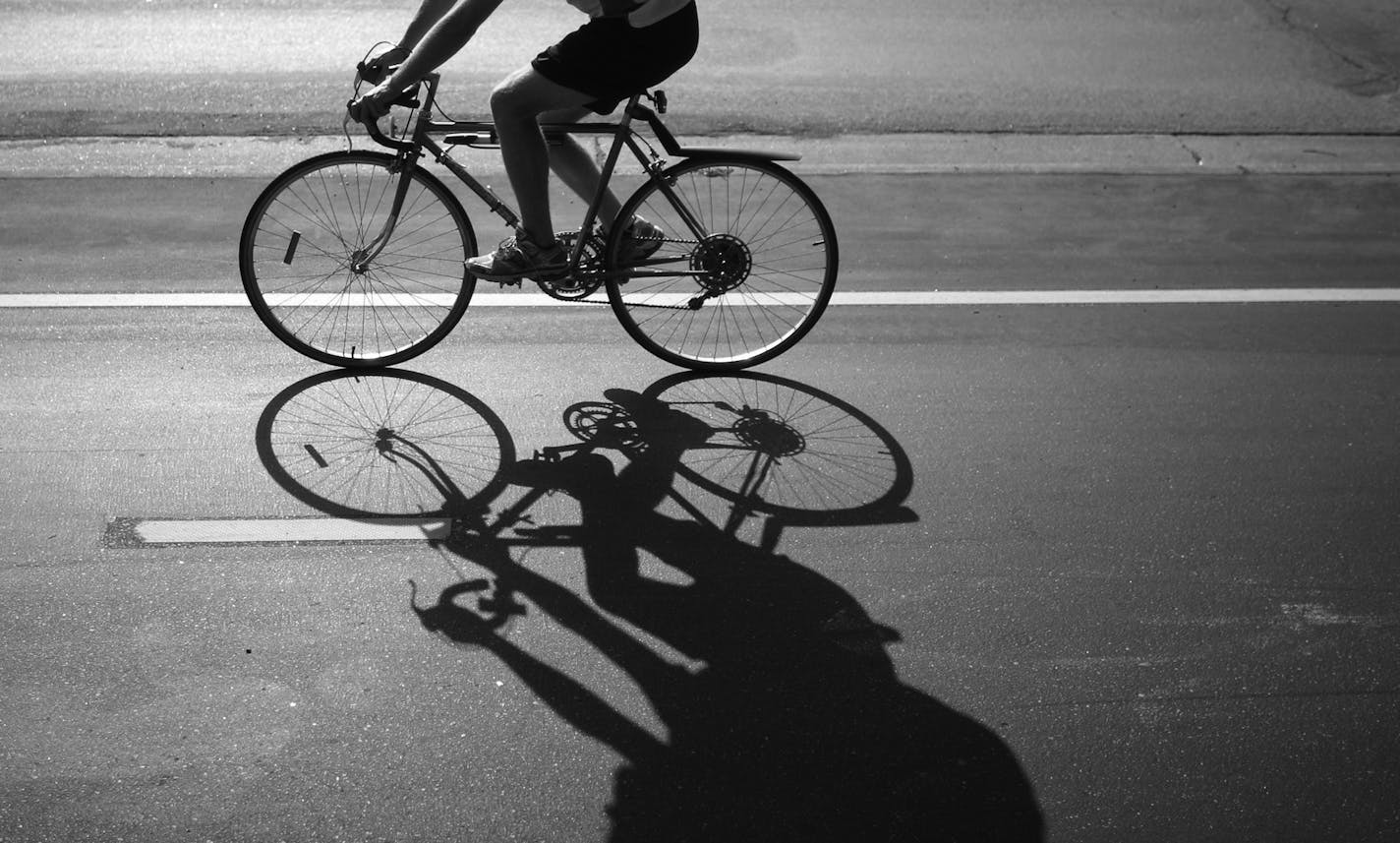 A bike casts a shadow as it rides along a road.