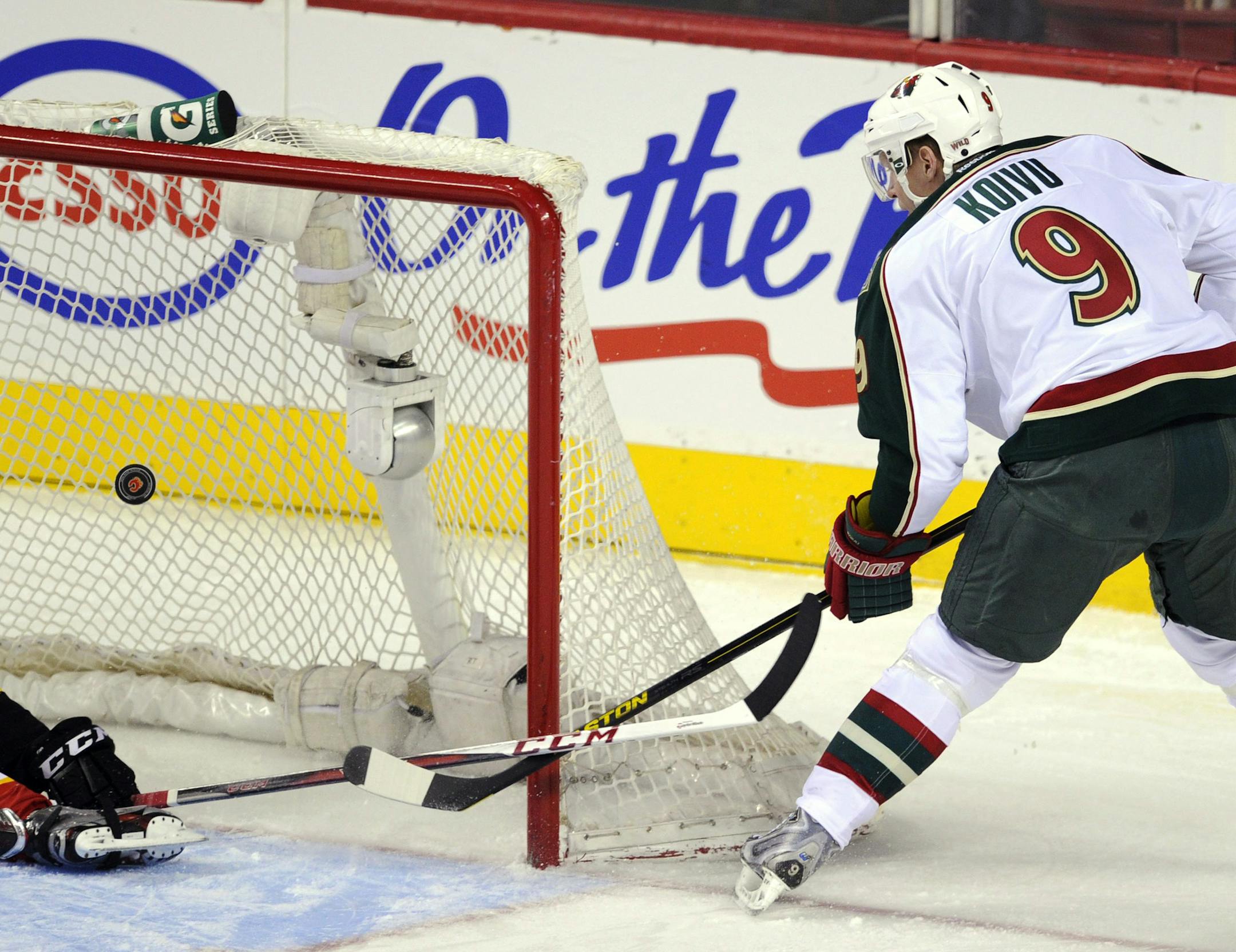 Minnesota Wild's' Mikko Koivu (9), of Finland, puts the puck past Calgary Flames' Mark Giordano for a goal during the first period of their NHL hockey game in Calgary, Alberta, Monday, April 15, 2013. (AP Photo/The Canadian Press, Larry MacDougal)