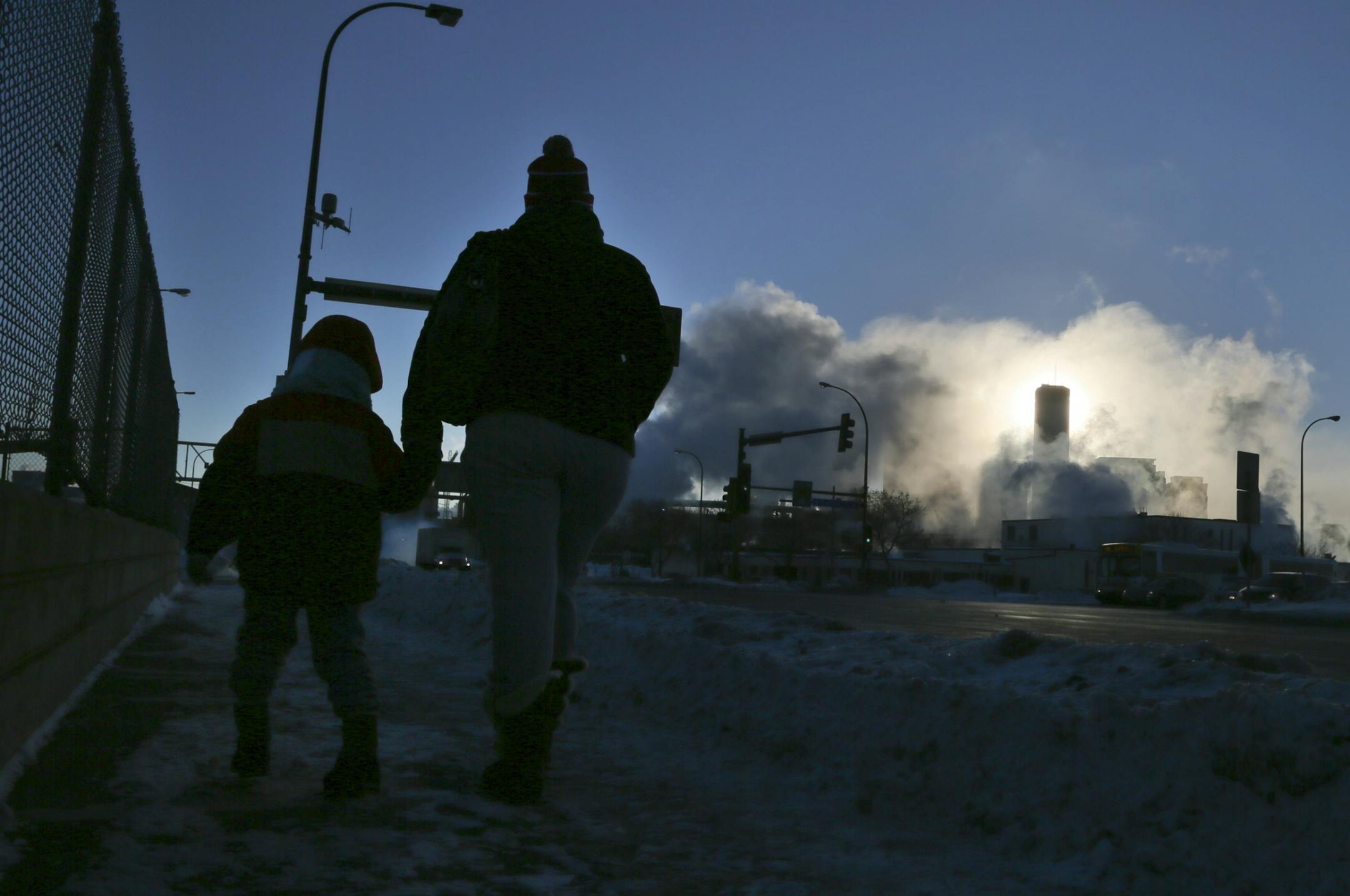 The collision of cold air and heat from car exhaust and steam from buildings is visible near Olson Memorial and Lyndale Ave. N. as a mother and child walk east along Olson Memorial Highway in Minneapolis on Thursday Jan. 23, 2014.