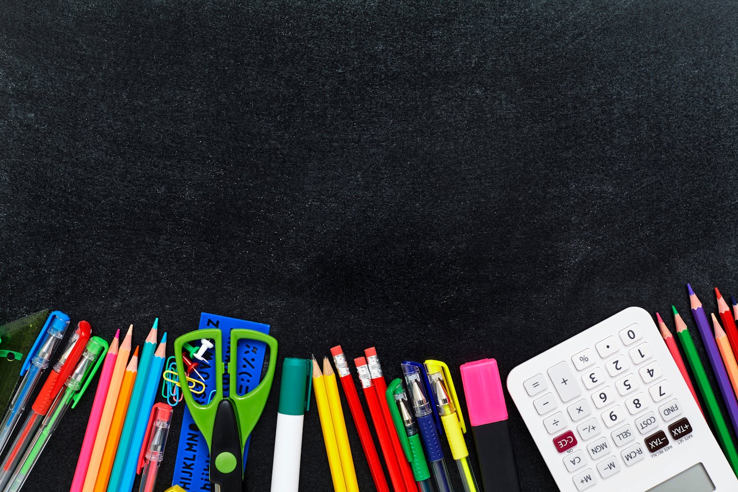 Directly above shot of school and office supplies. Stationeries are covering bottom of black surface. They are kept on blackboard.