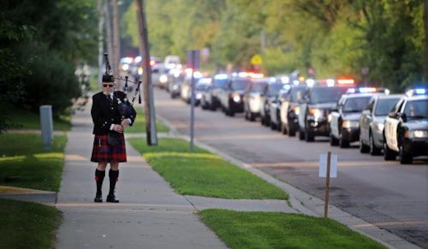 Bill Gilchrist with the Minnesota Police Pipe Band plays along Charlton St. as officers begin to gather at the funeral for Scott Patrick.