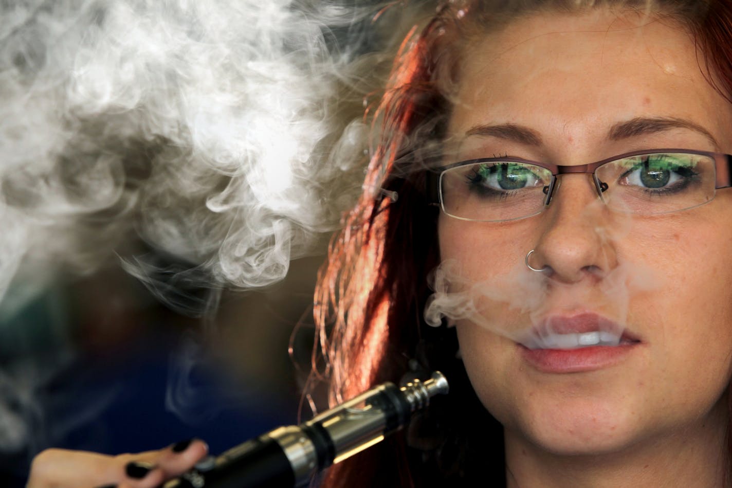 In this June 29, 2013 photo, Leah Overbaugh, a sales representative at the E Cig Crib in Coon Rapids, Minn., poses with a Siegelei e cigarette. Supporters of defining electronic cigarettes in the same light as traditional tobacco products won a key round Monday, May 5, 2014, in the Minnesota Legislature.