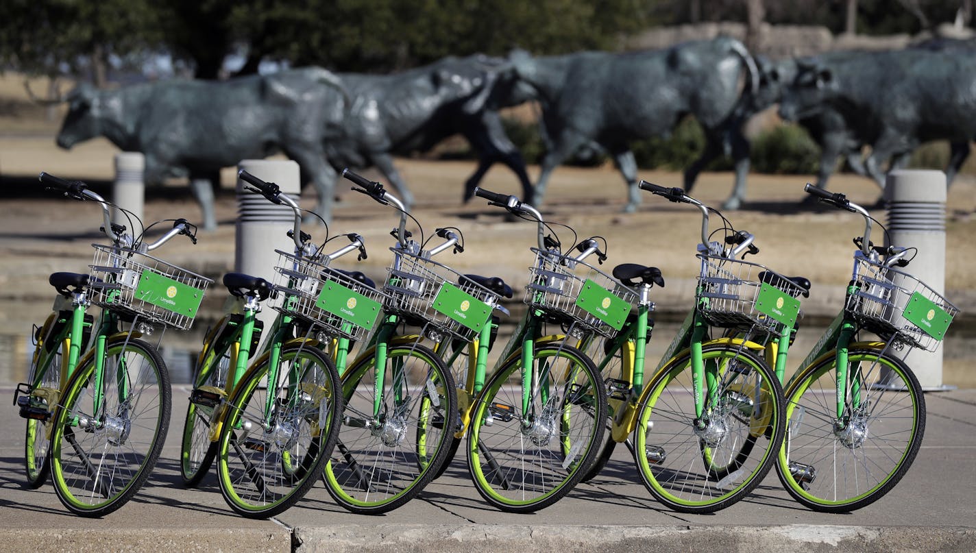 In this Feb. 8, 2018 photo, shared bikes ready to be used are lined up on a sidewalk by a popular tourist destination in Dallas. Shared bikes that can be left wherever the rider ends up are helping more people get access to the mode of transportation that reduces car traffic and increases exercise. But the dockless bikes are also producing some chaos with discarded bikes cluttering public spaces, blocking sidewalks and even placed in trees and lakes. Over the last year, startup companies have br