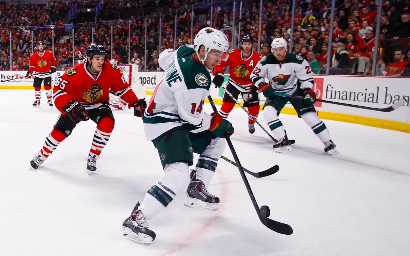 Minnesota Wild right wing Justin Fontaine (14) tries to control the puck in front of Chicago Blackhawks center Andrew Shaw (65) during the first period of an NHL hockey game in Chicago, Sunday, Jan. 11, 2015. (AP Photo/Kamil Krzaczynski)