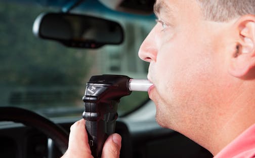 A male driver is blowing into an ignition interlock system which checks his alcohol concentration before allowing the vehicle to be started. Ignition interlock devices may be an alternative sentence for drunk driving or a probation requirement for those who have received a DUI.