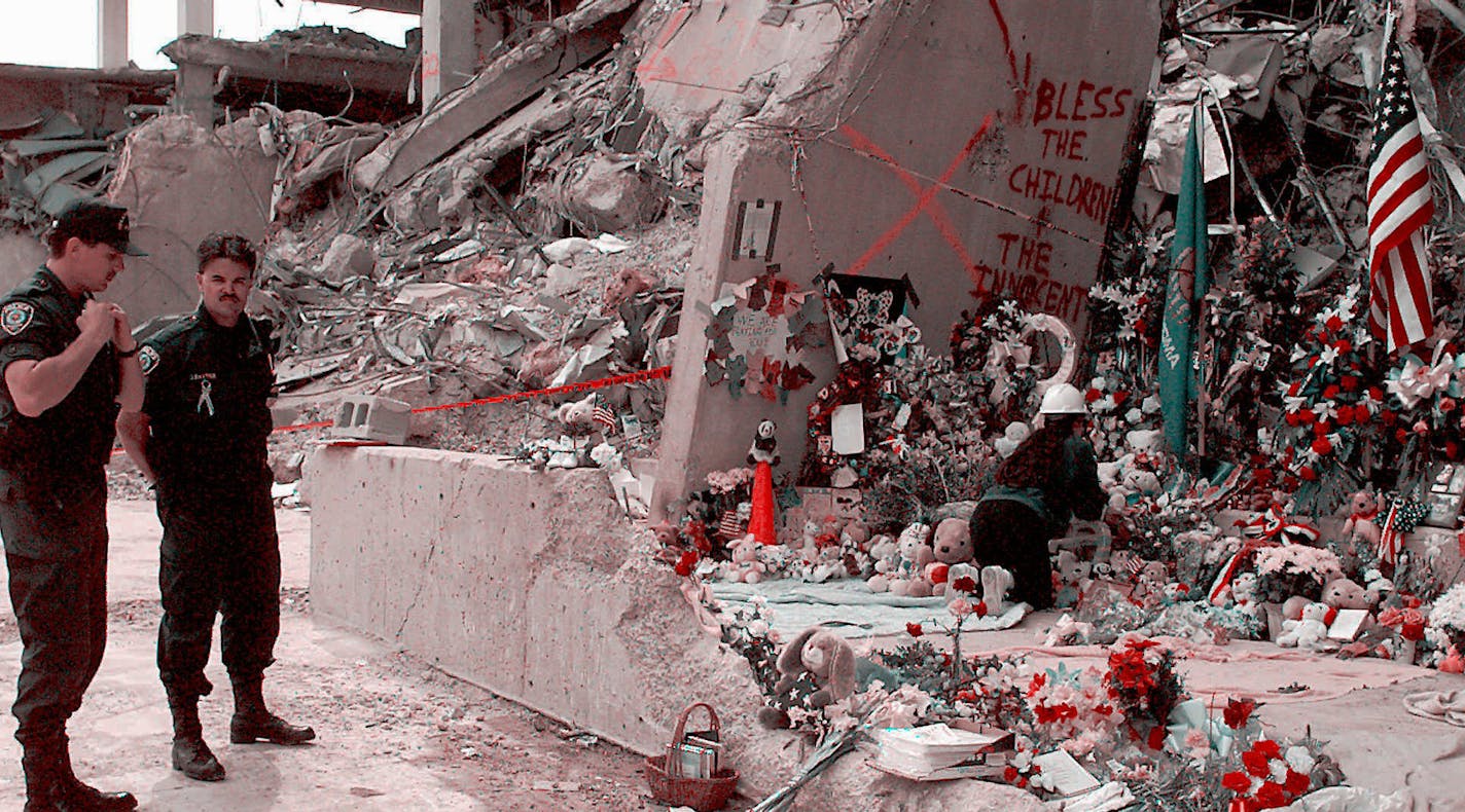 Officials stand near the Alfred P. Murrah Federal Building in Oklahoma City, Friday, May 5, 1995, as workers place flowers and memorial items at the scene fo the April 19, deadly car-bombing. The memorial items came from a makeshift memorial which had been built by mourners blocks away from the bomb site. Rescue crews ended their search for victims Thursday, with two bodies still missing. (AP Photo/J. Pat Carter) ORG XMIT: MIN2015041617113940