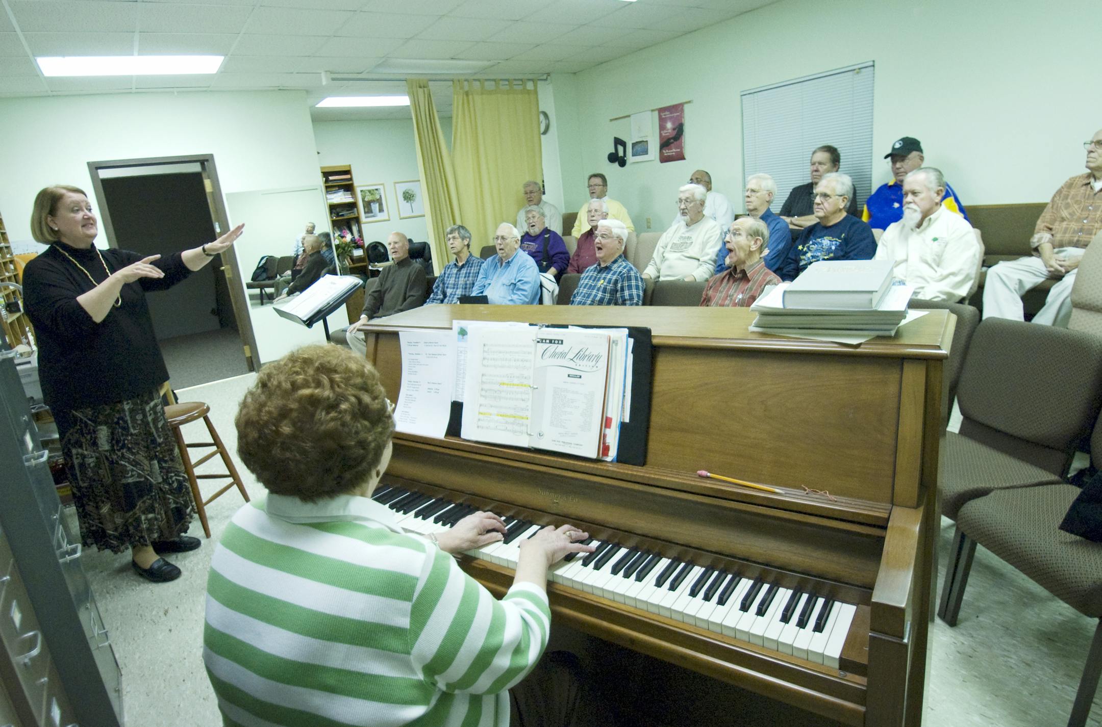 Photo by Liz Rolfsmeier Kathy Andrews led the Eagan Men's Chorus in a song, while IvaNell Monson, who has accompanied the group for 26 years, played the piano. The group considers their group favorite "Mighty Men of Music," as something of a theme song.