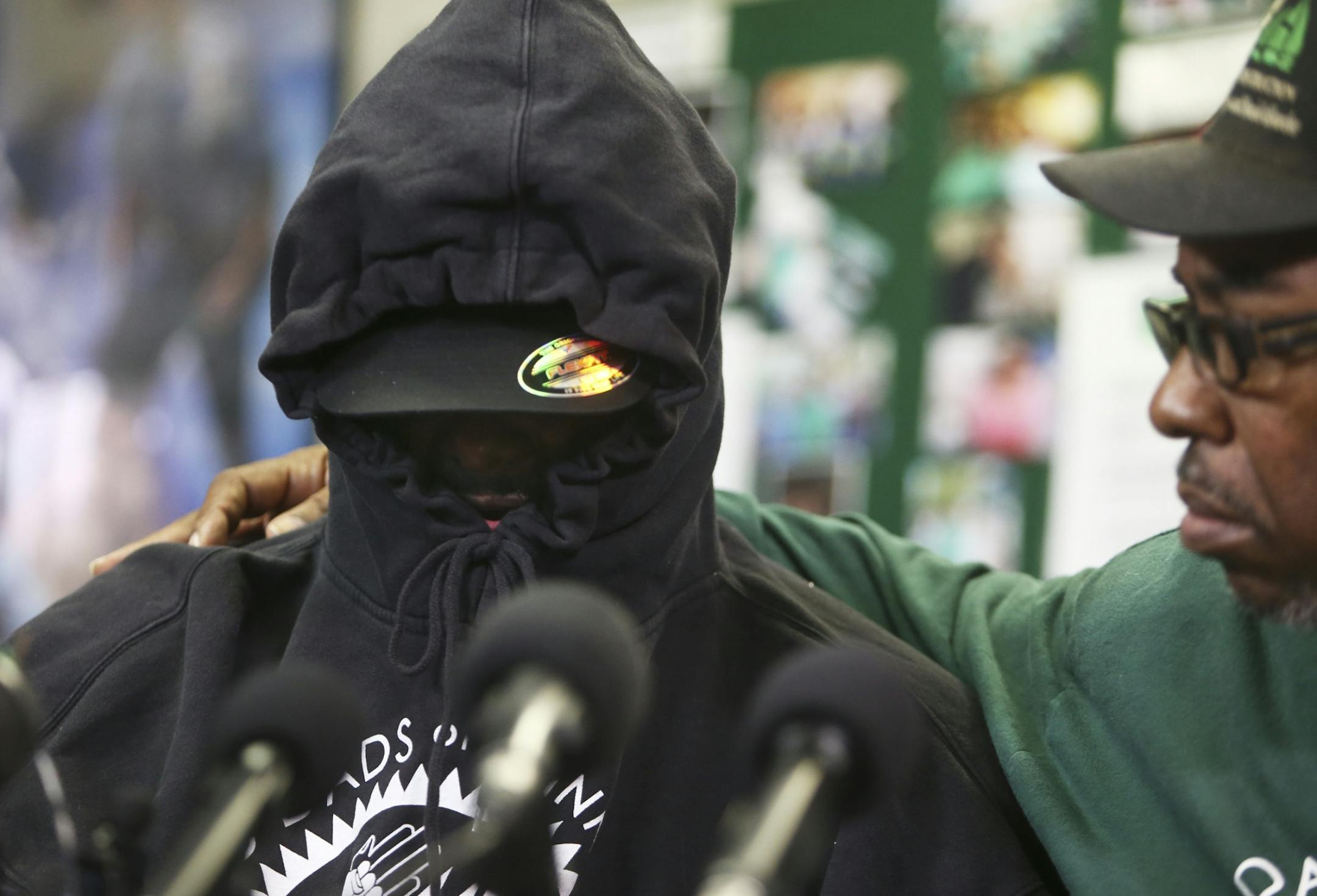 The father of 9-year-old plane stowaway, his face covered in a hoodie and hat to ensure his anonymity, talked to media members, sometimes through sobs, as he was accompanied by MAD DADS V.J. Smith, right, Wednesday, Oct. 9, 2013, a the MAD DADS office in Minneapolis, MN.(DAVID JOLES/STARTRIBUNE) djoles@startribune.com His face covered in a hoodie and hat to ensure his anonymity the father of 9-year-old plane stowaway talk with media members at the office of MadDads at their Lake Street office We