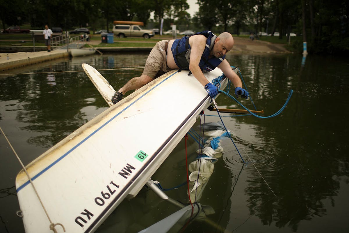 Martin Conroy got a rope squared away as he waited for some help from others as they attempted to right his overturned sailboat on Lake Nokomis Sunday