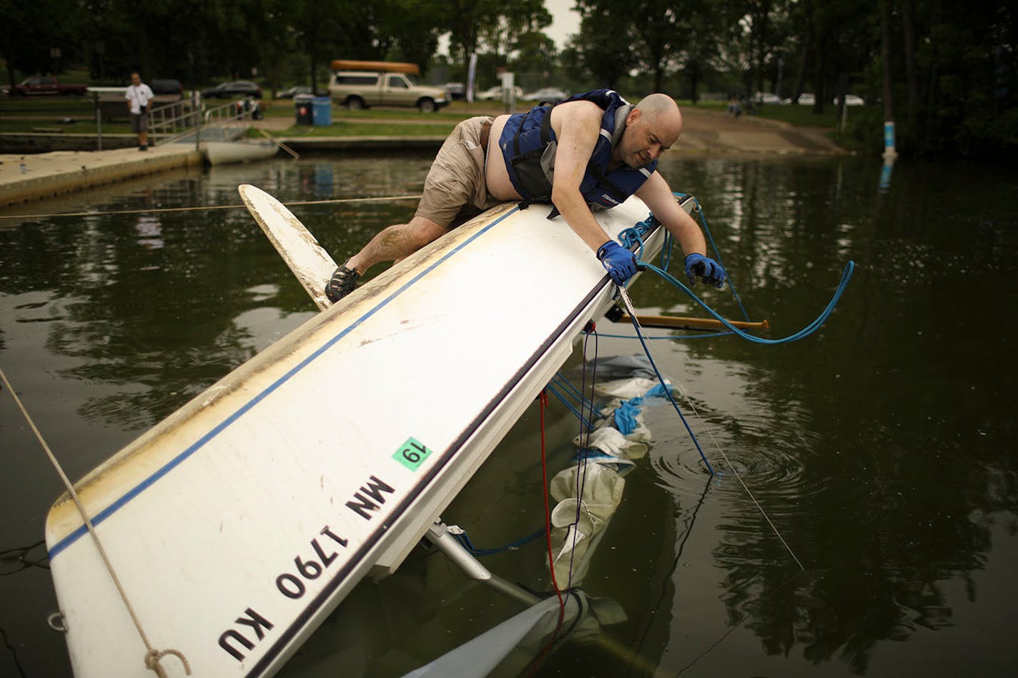 Martin Conroy got a rope squared away as he waited for some help from others as they attempted to right his overturned sailboat on Lake Nokomis Sunday afternoon. When he drove past the lake after the storm Sunday morning, "I saw that I was the only one flipped, so I went home and changed for my unplanned afternoon adventure."