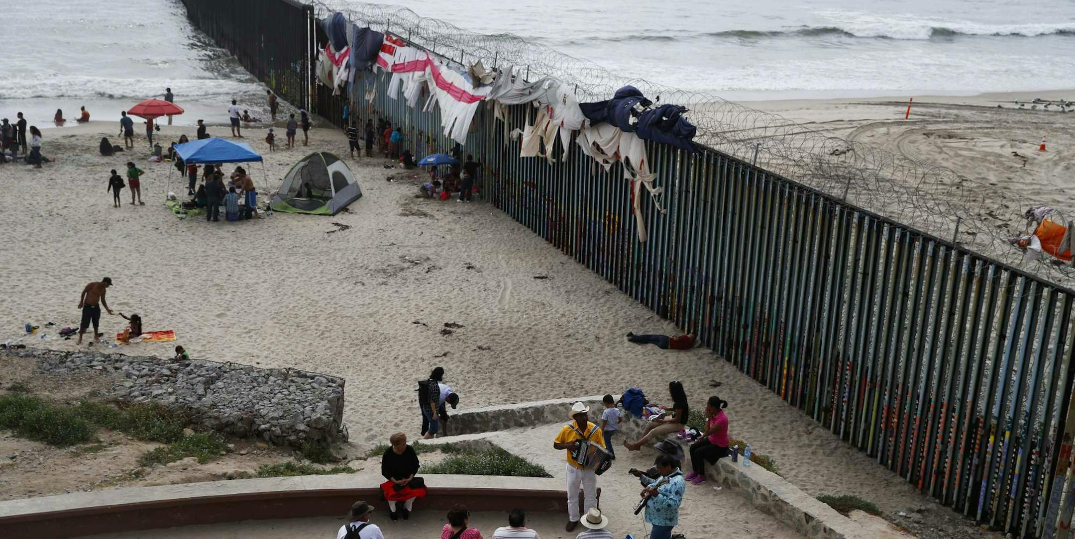 Musicians play music next to the U.S. border wall topped with razor wire in Tijuana, Mexico, Sunday, June 9, 2019. (AP Photo/Eduardo Verdugo)