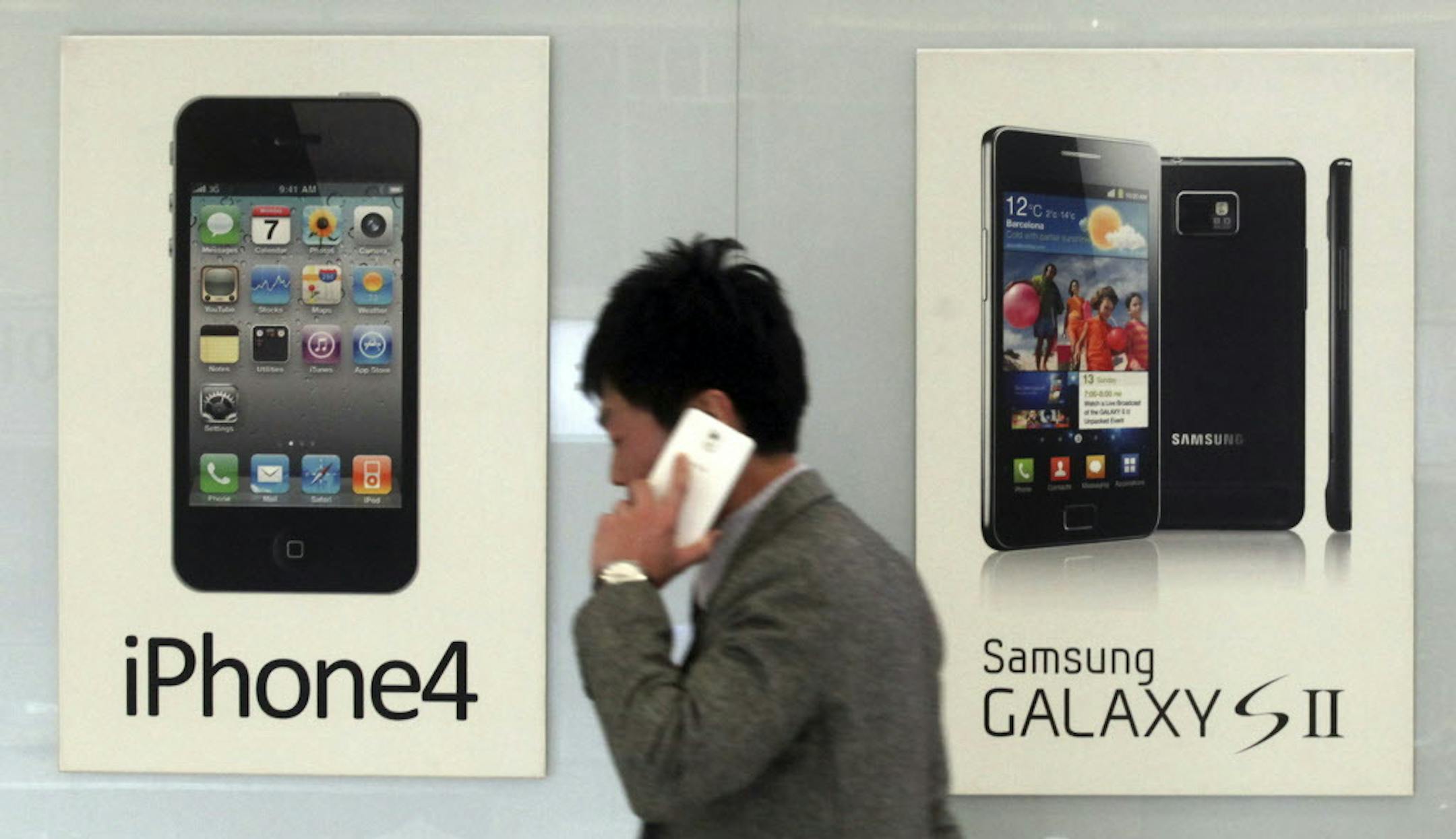 FILE - In this Nov. 22, 2013 file photo, a man walks past banners advertising smartphones by Samsung and Apple at a mobile phone shop in Seoul, South Korea. The high-stakes battle between the world's largest smartphone makers is scheduled to wrap up this week after a monthlong trial that has pulled the curtain back on just how very cutthroat the competition is between Apple and Samsung. Closing arguments in the patent-infringement case are scheduled to begin Monday, April 28, 2014 with the two t