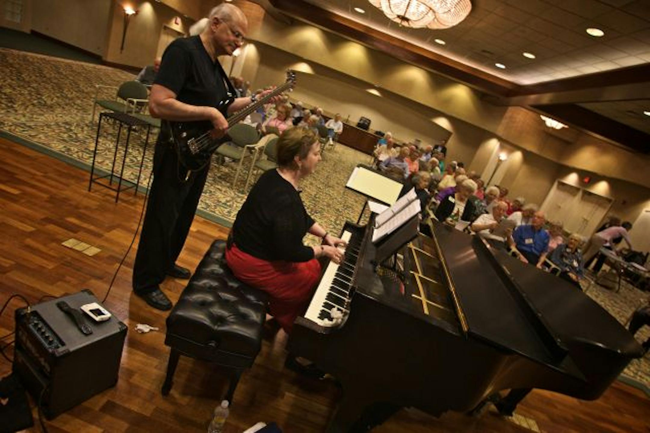 Jeanie Brindley-Barnett plays the piano and sings, as her husband Steve Barnett plays the bass as they led residents of Friendship Village in voice exercises, elocution and sing-alongs, including basic two-part harmony.