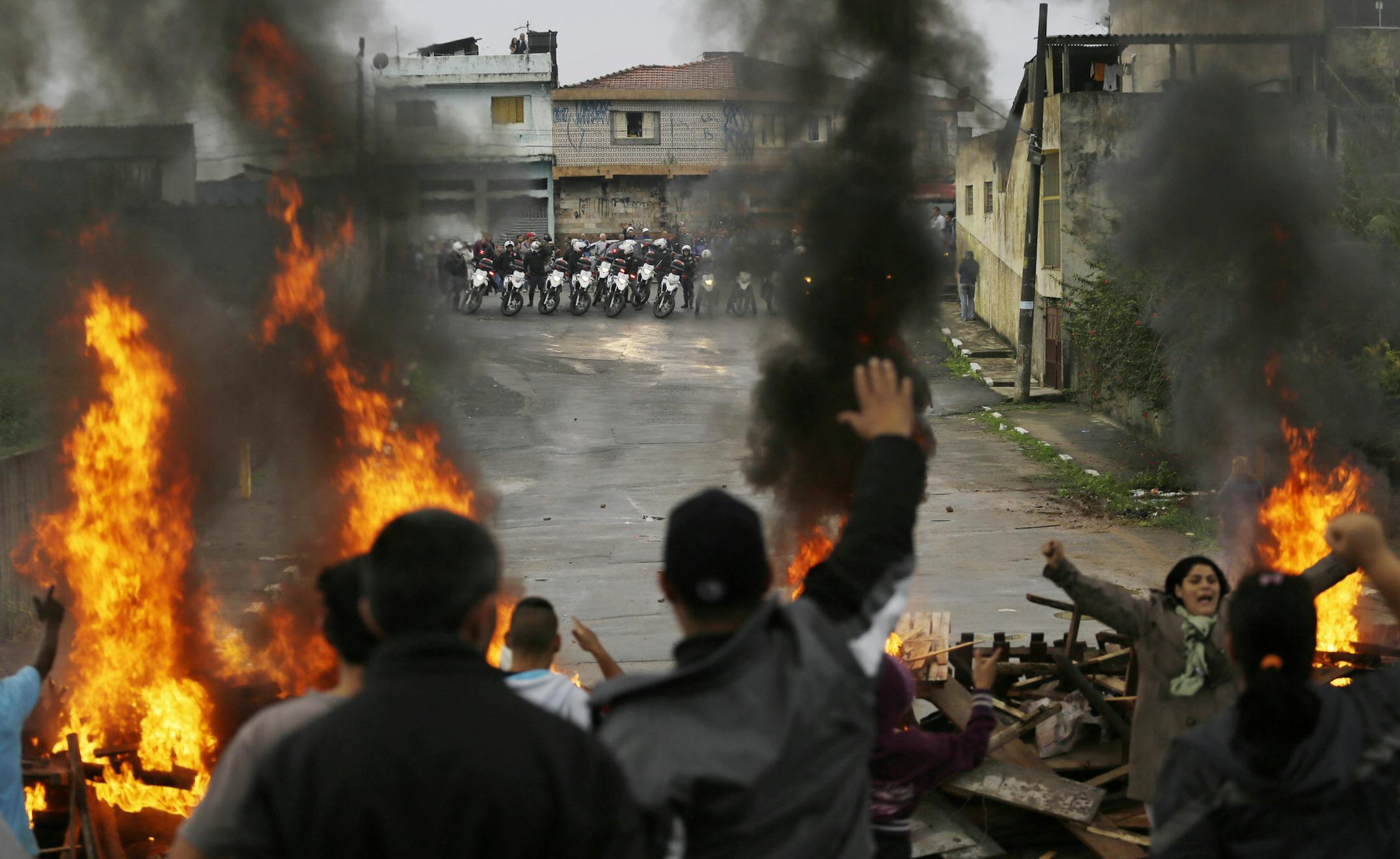 Residents shout slogans against police as they set a roadblock on fire to fight their eviction from the Parque Sao Rafael neighborhood in Sao Paulo, Brazil, Thursday, June 27, 2013. Police are evicting more than 100 families from this private property which has been illegally occupied for about one year. The land is located far away from infrastructure related to the upcoming World Cup and Olympic games. (AP Photo/Nelson Antoine)